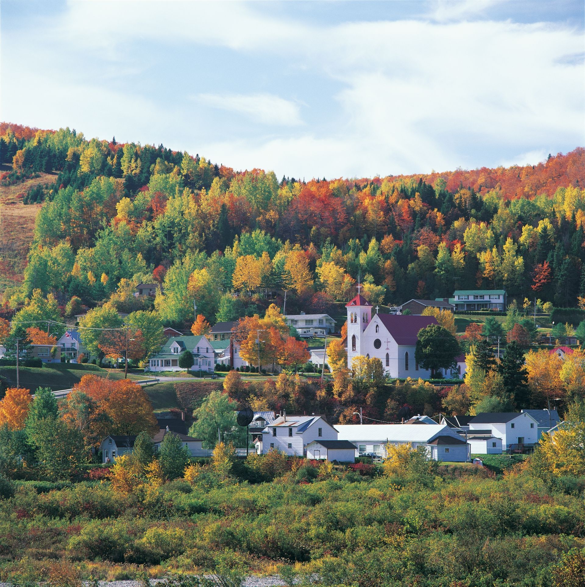 Het dorpje Matapedia in Quebec, Canada, in de herfst, gelegen op een heuvel met witte huizen en een kerk, onder kleurrijke, beboste heuvels.