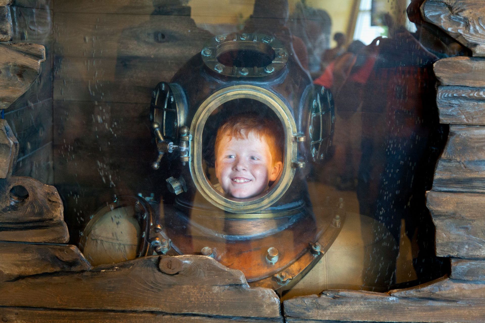 Een kind lacht in een rond patrijspoortje op een achtergrond van een vintage houten schip.