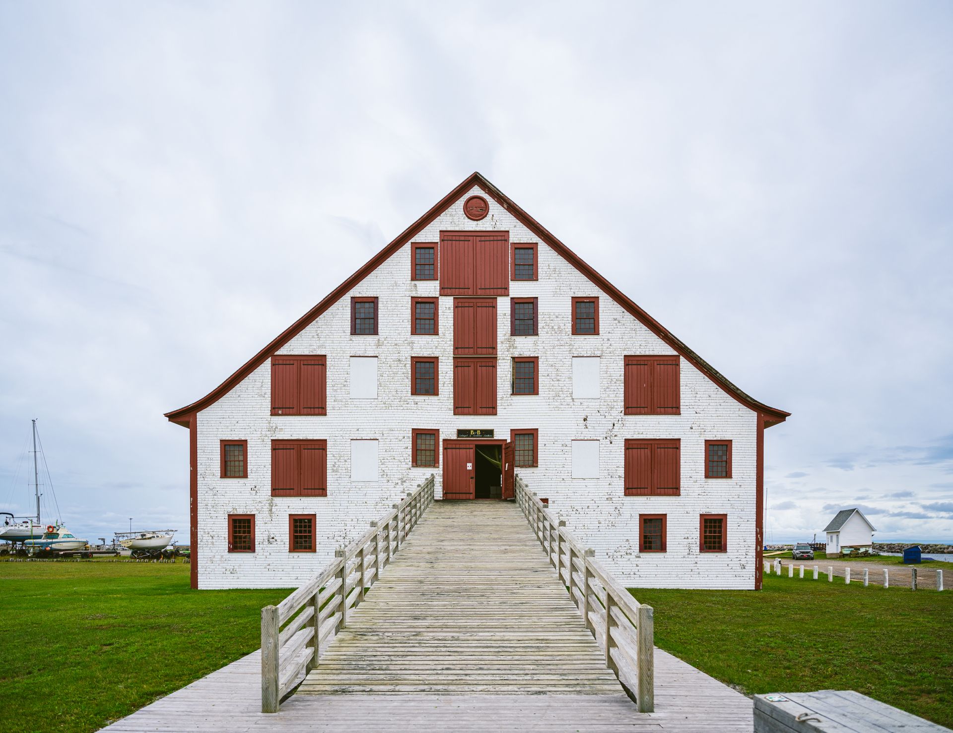 Het historische witte gebouw van The LeBoutillier Warehouse in Quebec, Canada met rood omlijste ramen en een centrale trap op een grasveld.