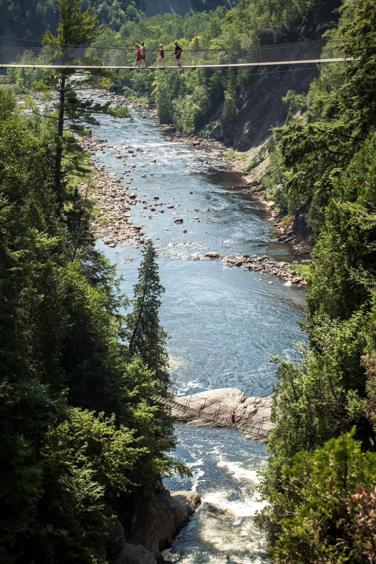 Hangbrug over de beboste rivierkloof Canyon Sainte-Anne in Canada met twee mensen die boven het kolkende water oversteken.