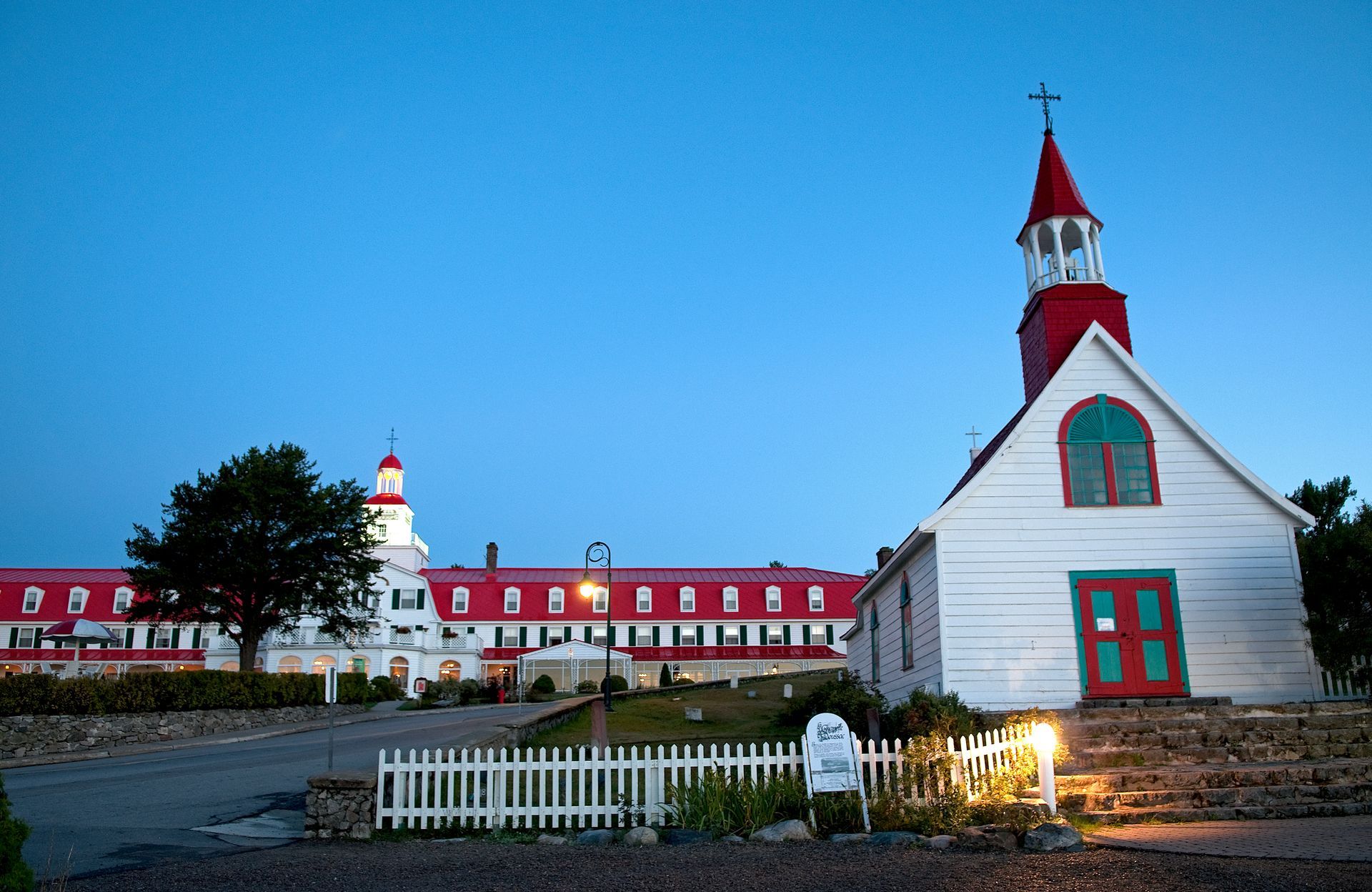 Hotel Tadoussac met rode daken in de schemering, met een kleine kerkachtige toren en een wit hek.