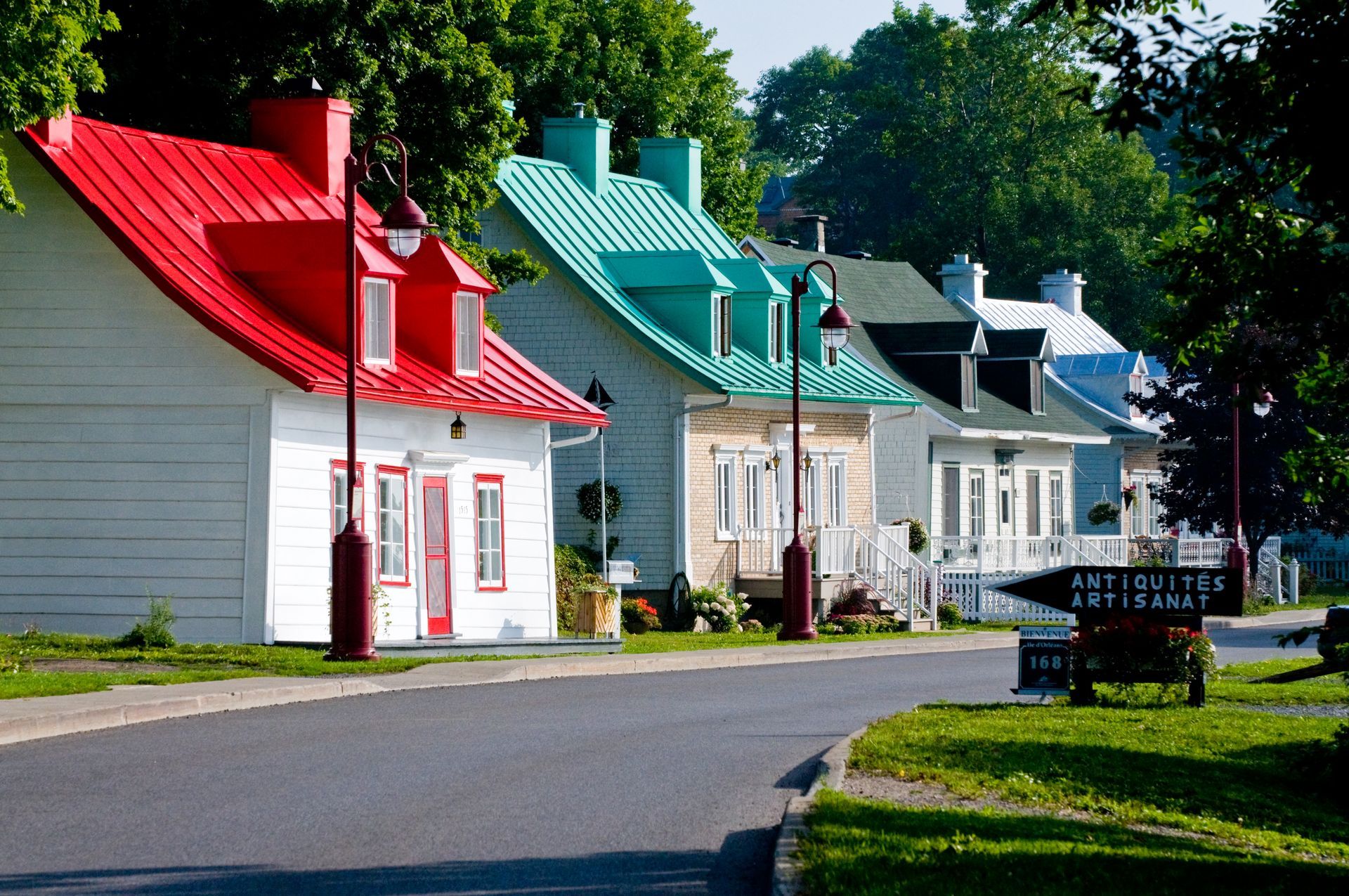 Kleurrijke, historische huizen met rode, turquoise en witte daken op le d'Orléans in Canada staan langs een rustige straat onder de bomen.