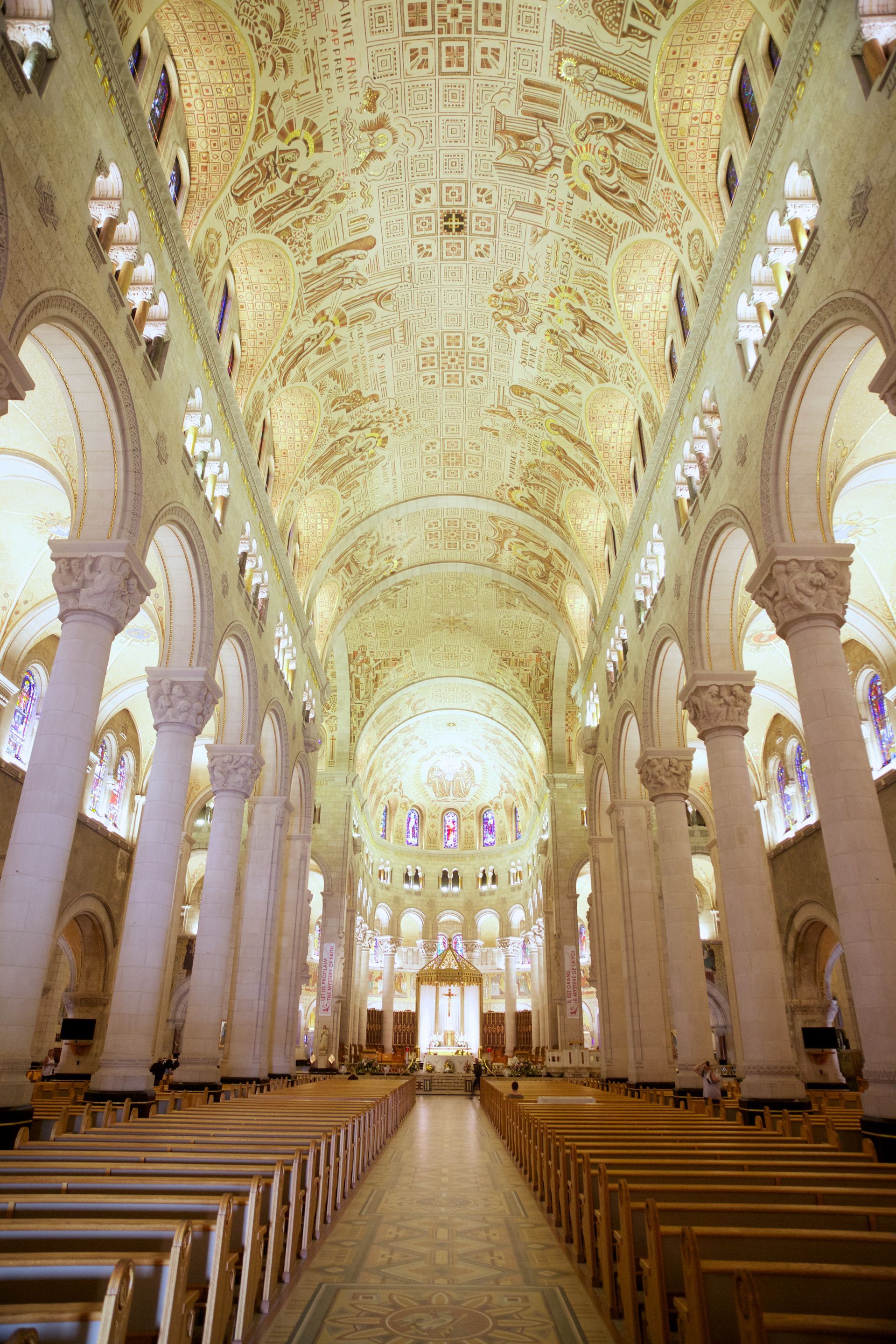 De rijk versierde kathedraalinterieur van Sanctuaire Notre-Dame de Sainte-Anne-de-Beaupré in Canada met een gouden gewelfd plafond, witte zuilen en rijen houten kerkbanken.