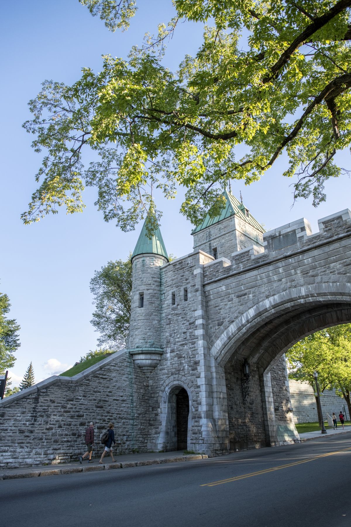Stenen stadspoort Laporte Saint-Louis in Quebec met boogvormige ingang en groene torens onder een blauwe hemel vol bomen.