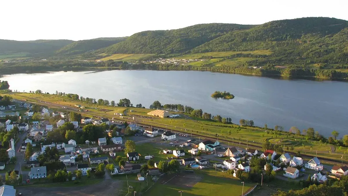 Het stadje Lac-au-Saumon in Quebec, Canada, in een rivierdal met huizen aan de oevers van een breed meer en groene heuvels bij zonsondergang.