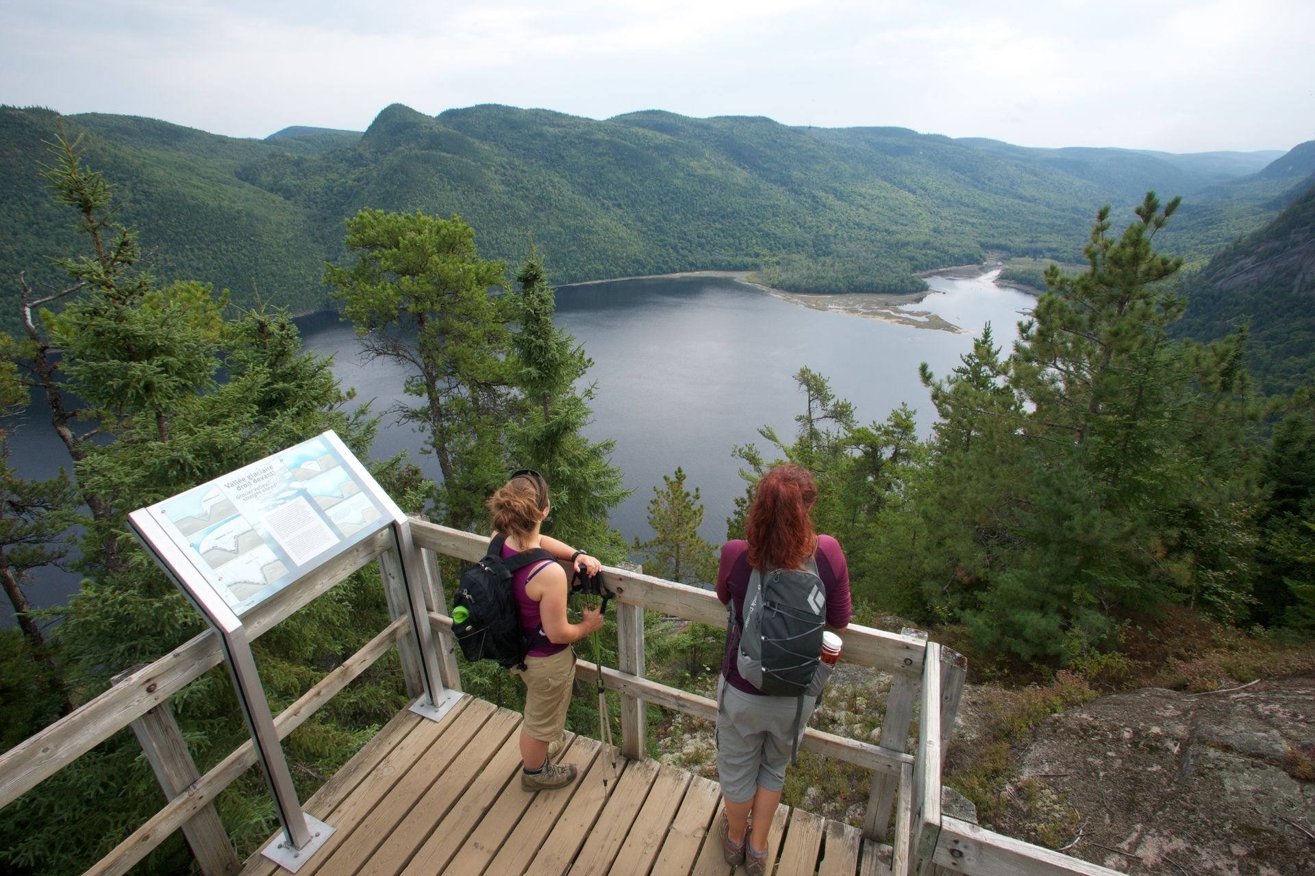 Twee wandelaars op een schilderachtig uitzichtpunt in Parc national du Fjord-du-Saguenay in Canada boven een meer, omgeven door groene bergen.