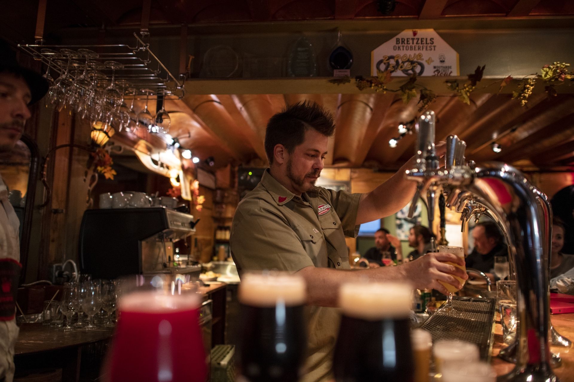 Een barman in Mauricie, Canada, schenkt een drankje in achter een glanzende bar met warme verlichting en biertaps.
