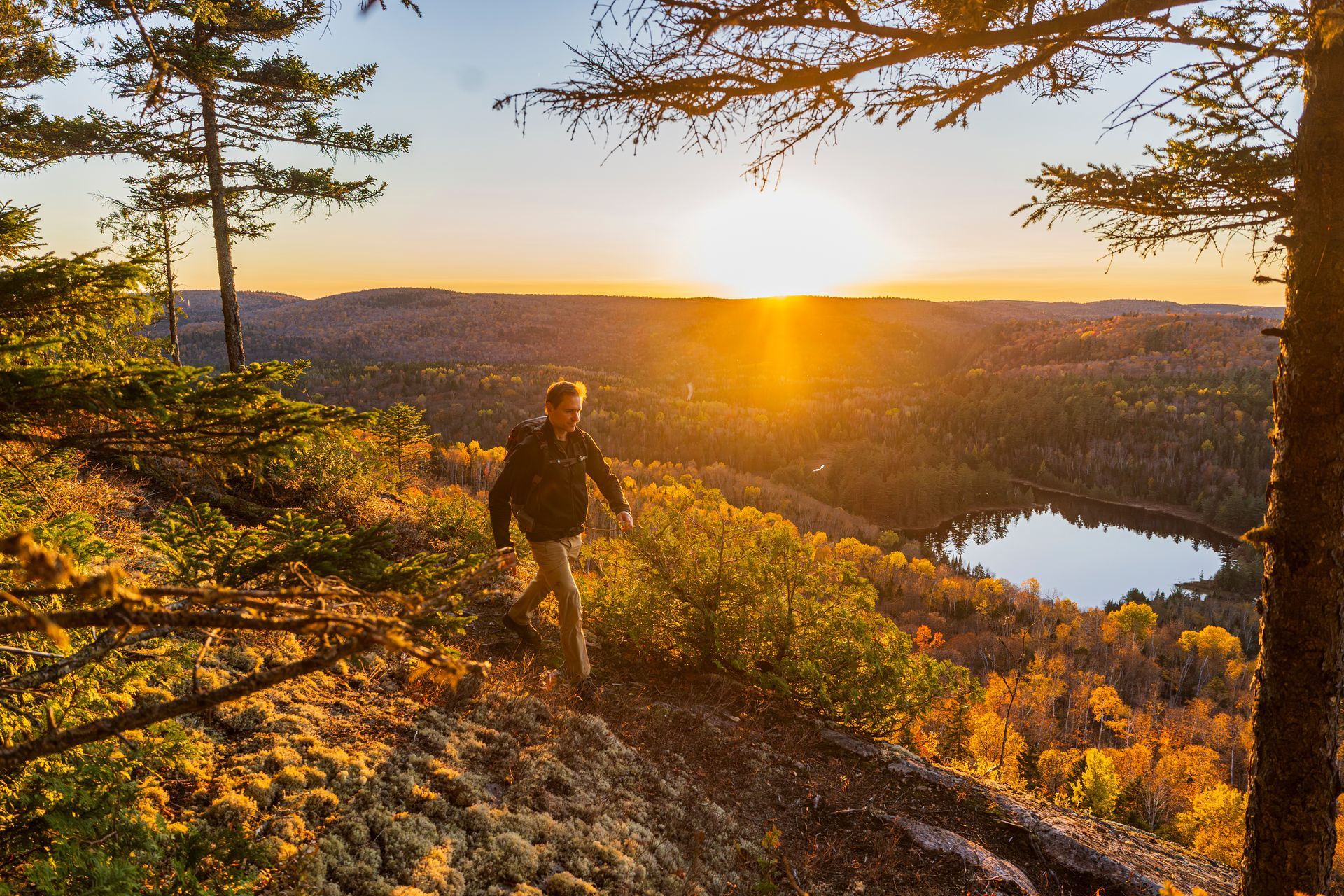 Wandelaar in Mauricie, Canada, op een rotsachtige bergkam bij zonsondergang, met uitzicht op een rivier en een herfstbos.