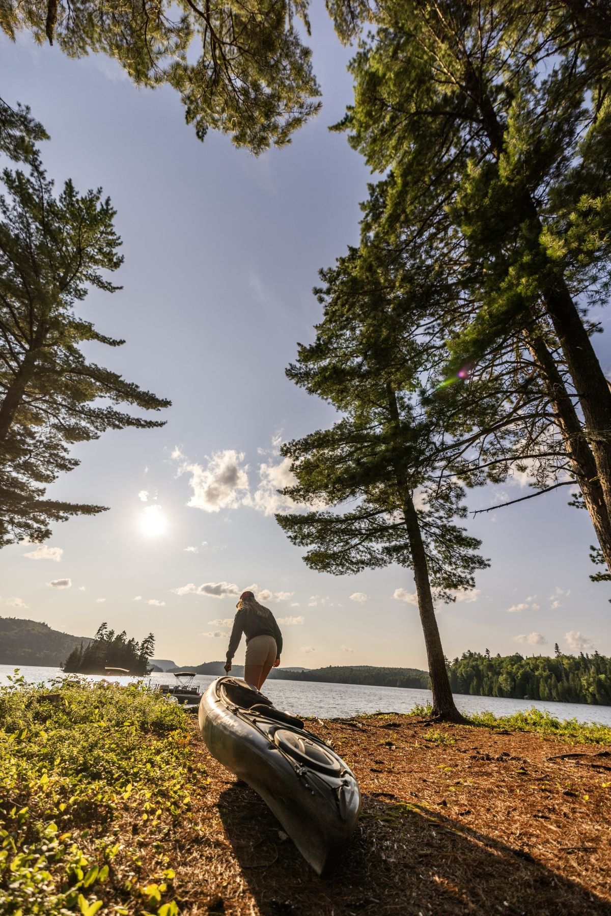 Een persoon laadt een kano in bij een zonnige oever van een meer in Mauricie, Canada, met bomen op de achtergrond en een andere kano op de voorgrond.