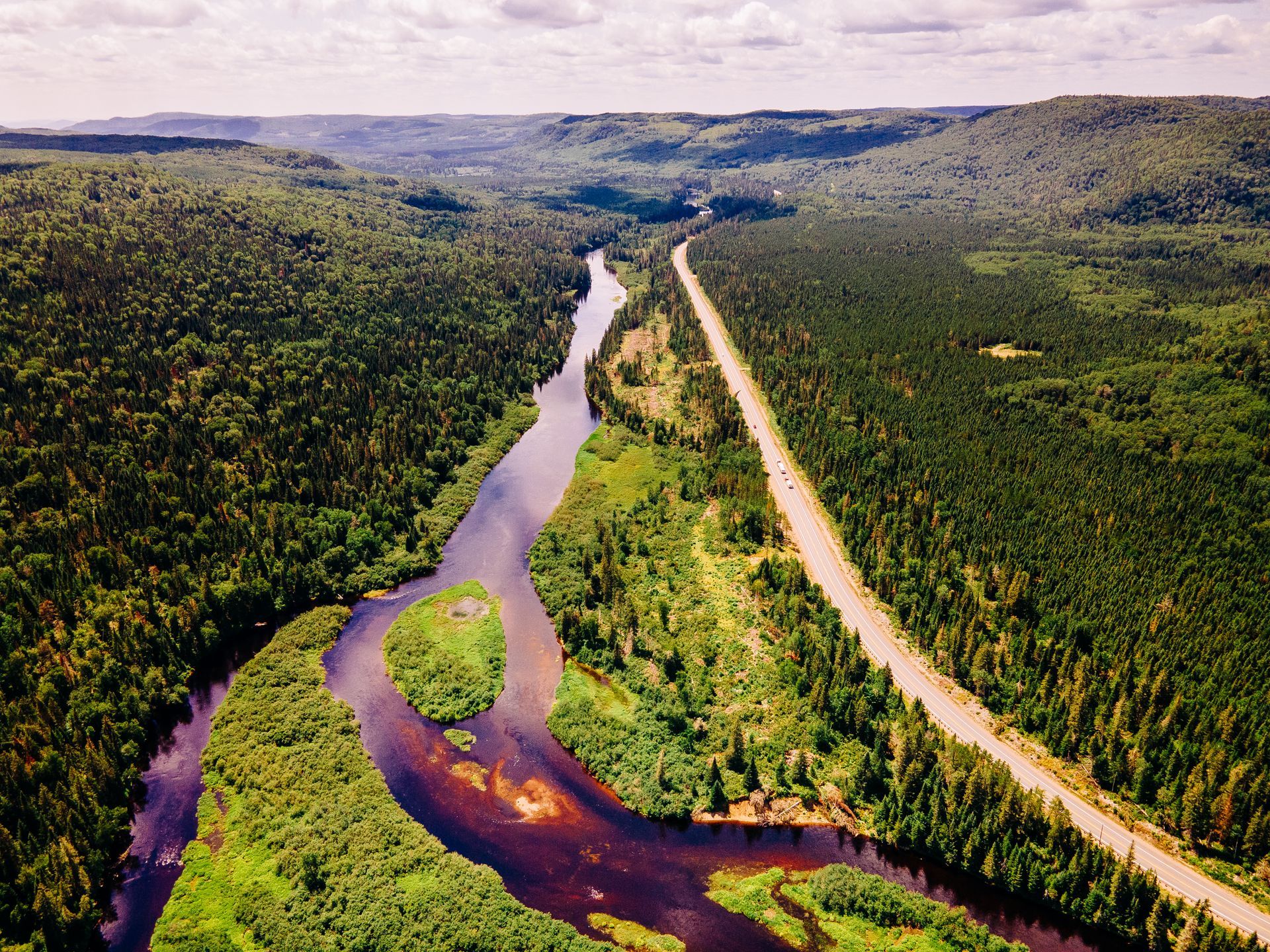 Een kronkelende rivier in Mauricie, Canada, door een dicht groen bos, langs een onverharde weg onder een bewolkte hemel.