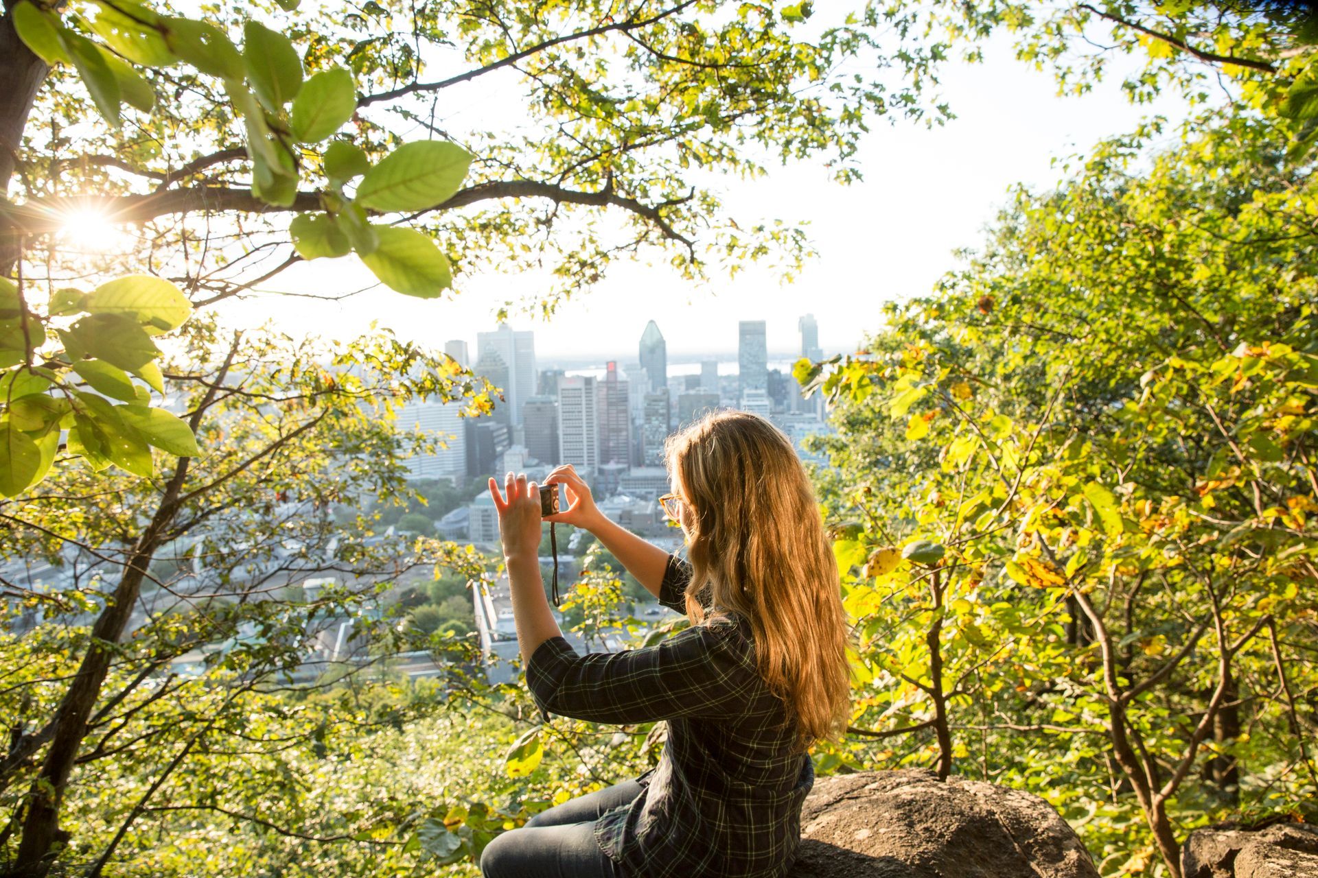 Iemand fotografeert de skyline van Montréal vanaf een lommerrijke heuveltop bij zonsondergang.