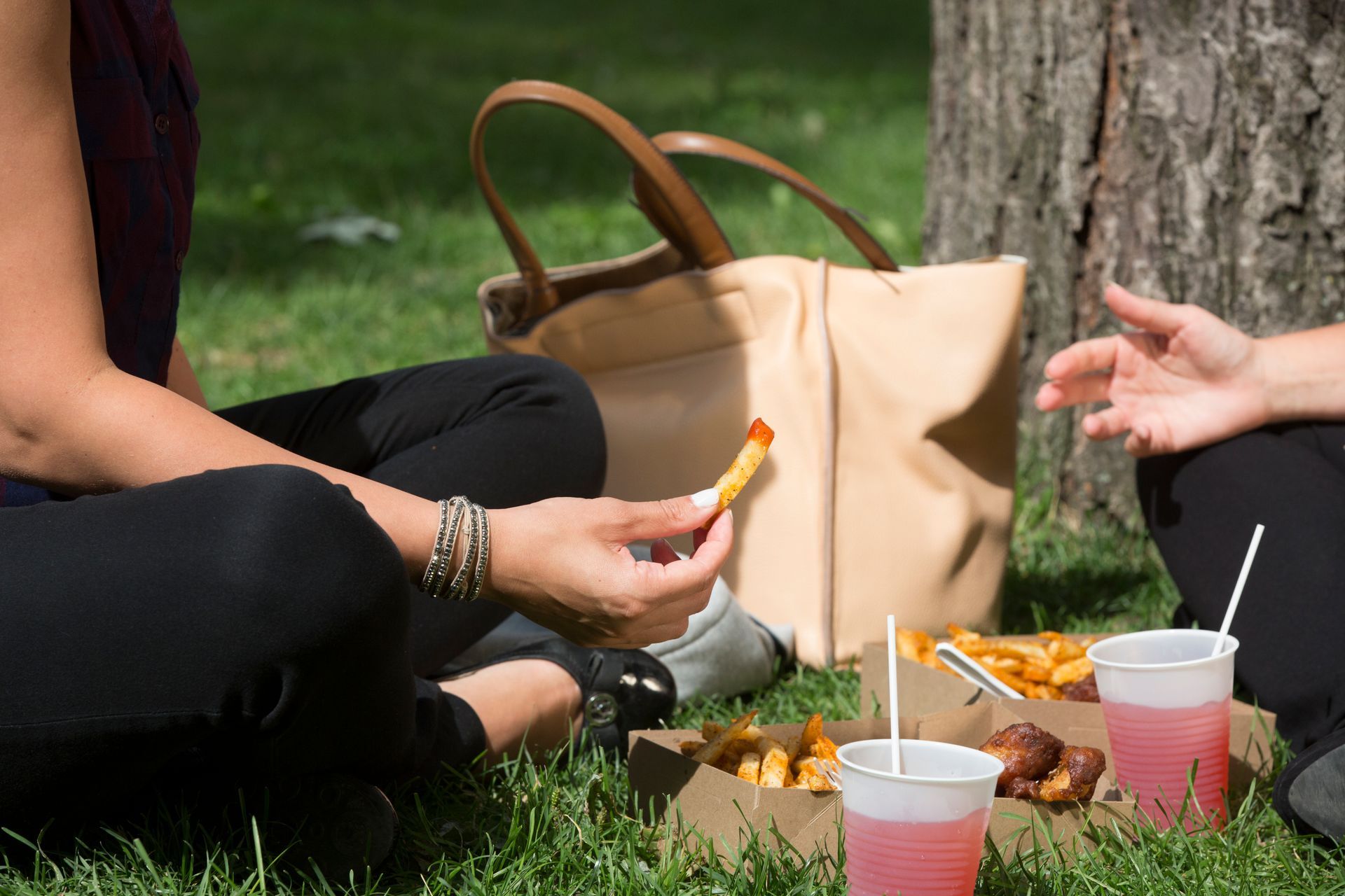 Mensen zitten op het gras in Montreal met een picknickmand, met een snack naast drankjes en een beige tas.