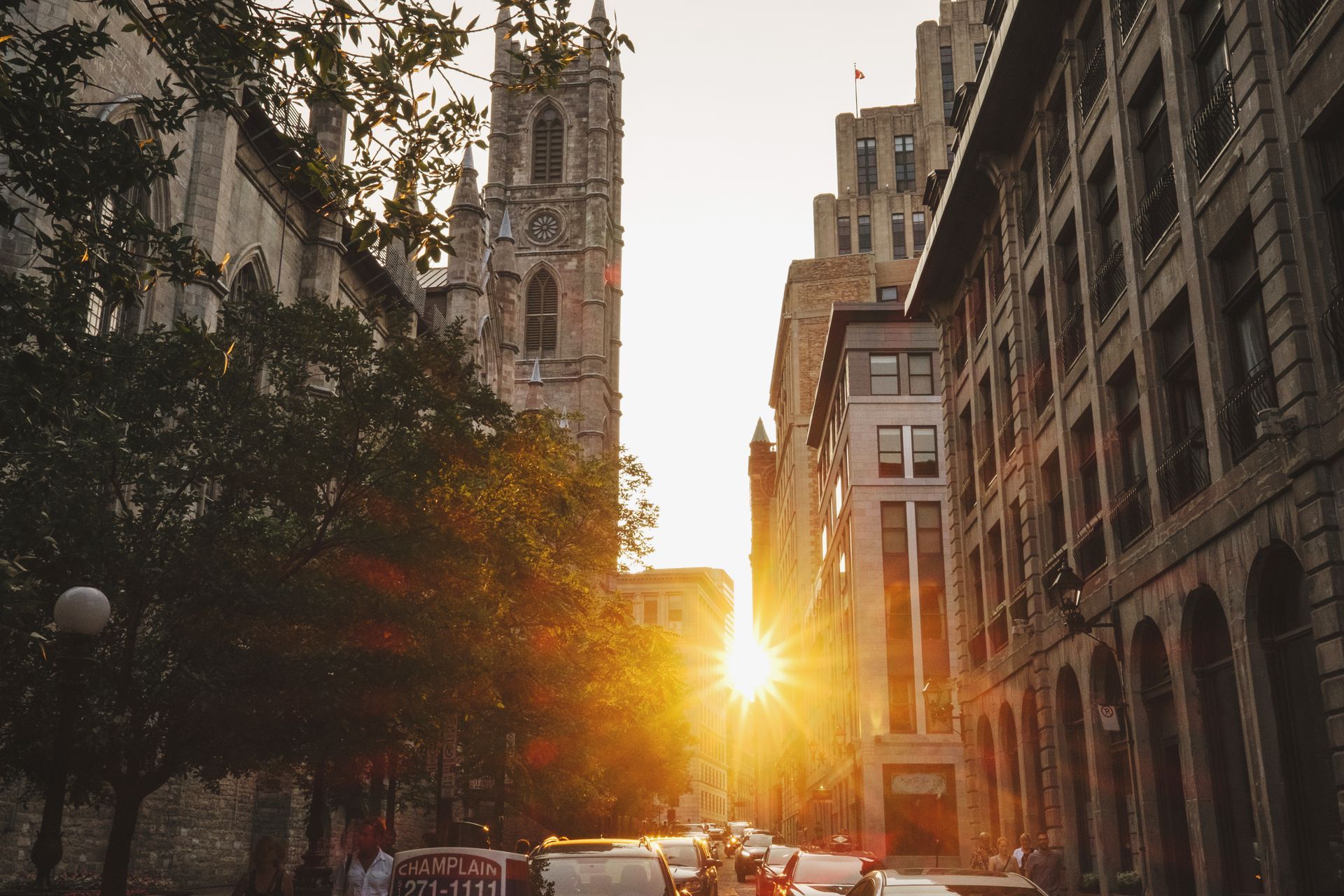 Zonsondergang boven een stadsstraat in Montreal met hoge historische gebouwen en bomen langs de weg.