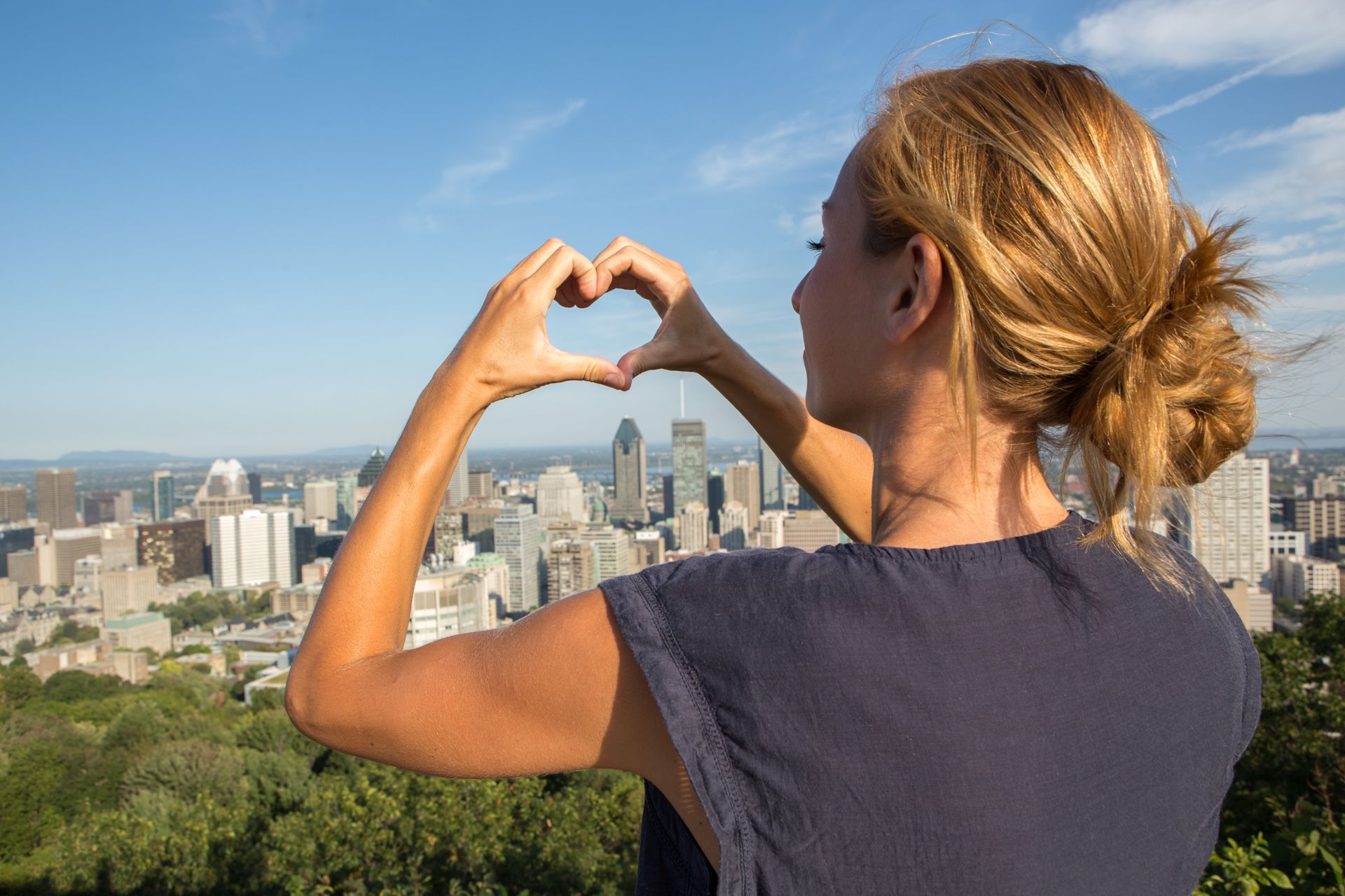 Iemand die met zijn handen een hartje vormt terwijl hij op een zonnige dag naar de skyline van Montreal kijkt.
