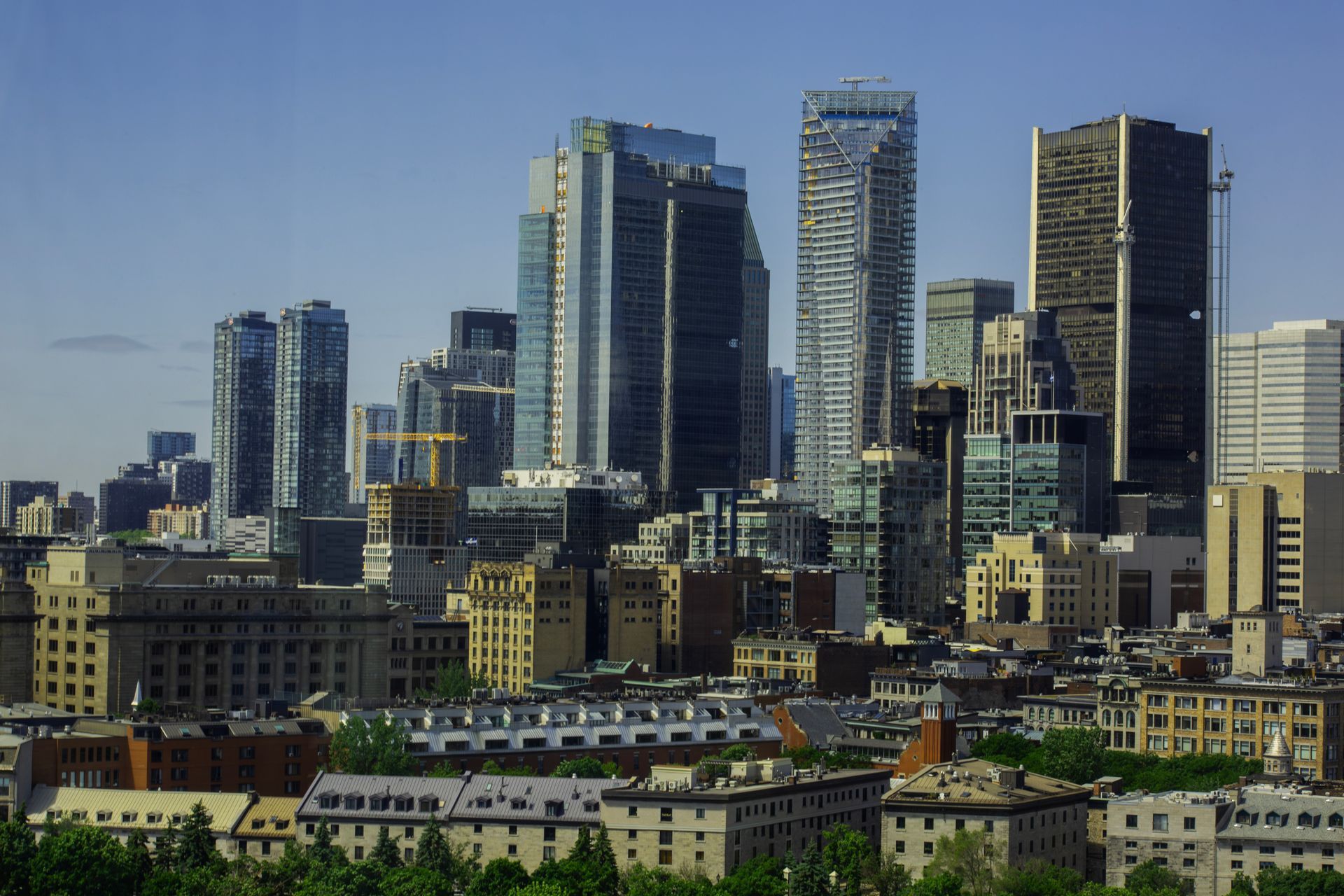 Moderne stadsgezicht van Montreal met hoge glazen wolkenkrabbers en lage gebouwen onder een helderblauwe hemel.