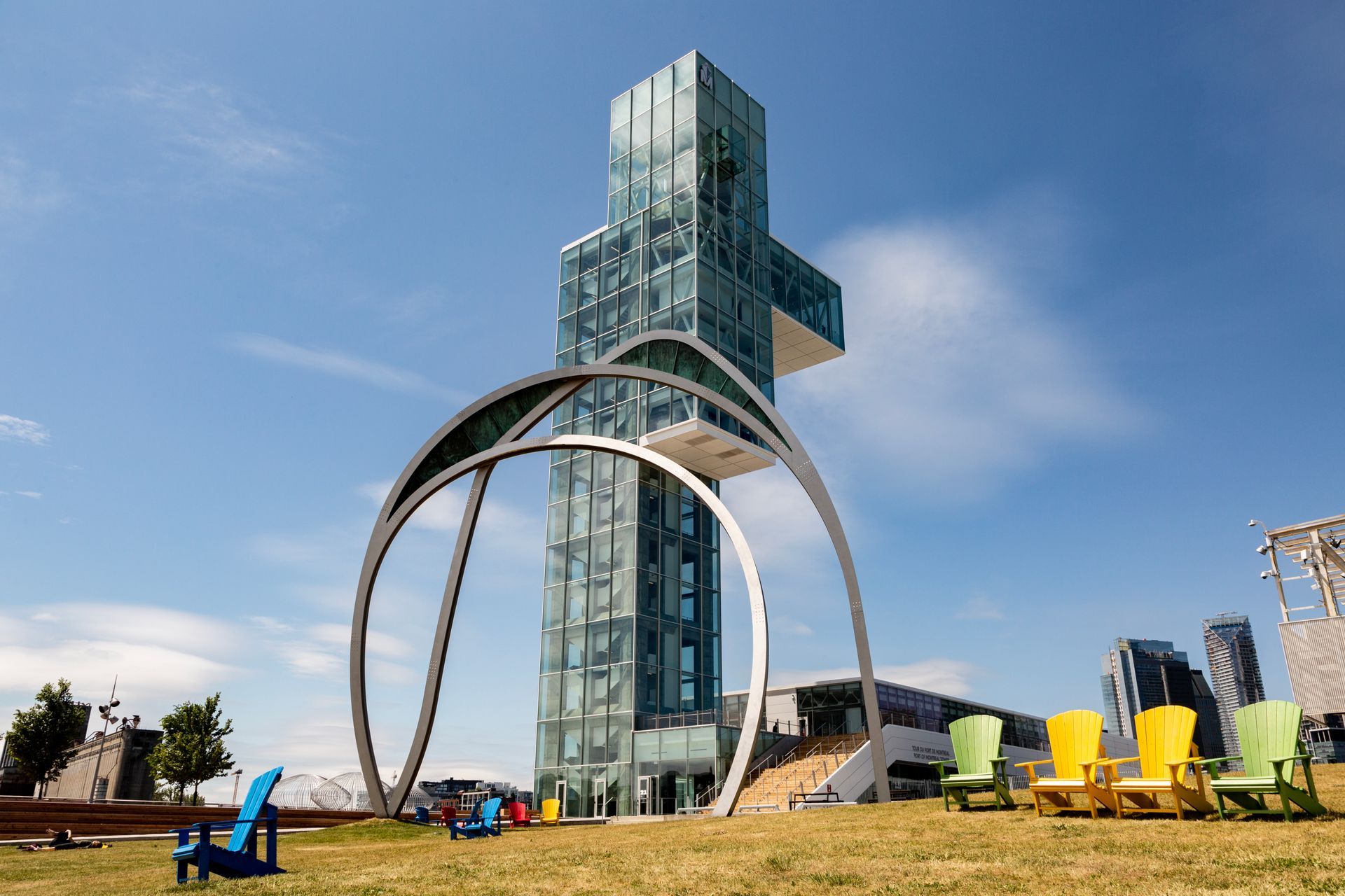 De Montreal Tower in Montreal achter een grote ronde metalen sculptuur op een grasveld met kleurrijke stoelen.
