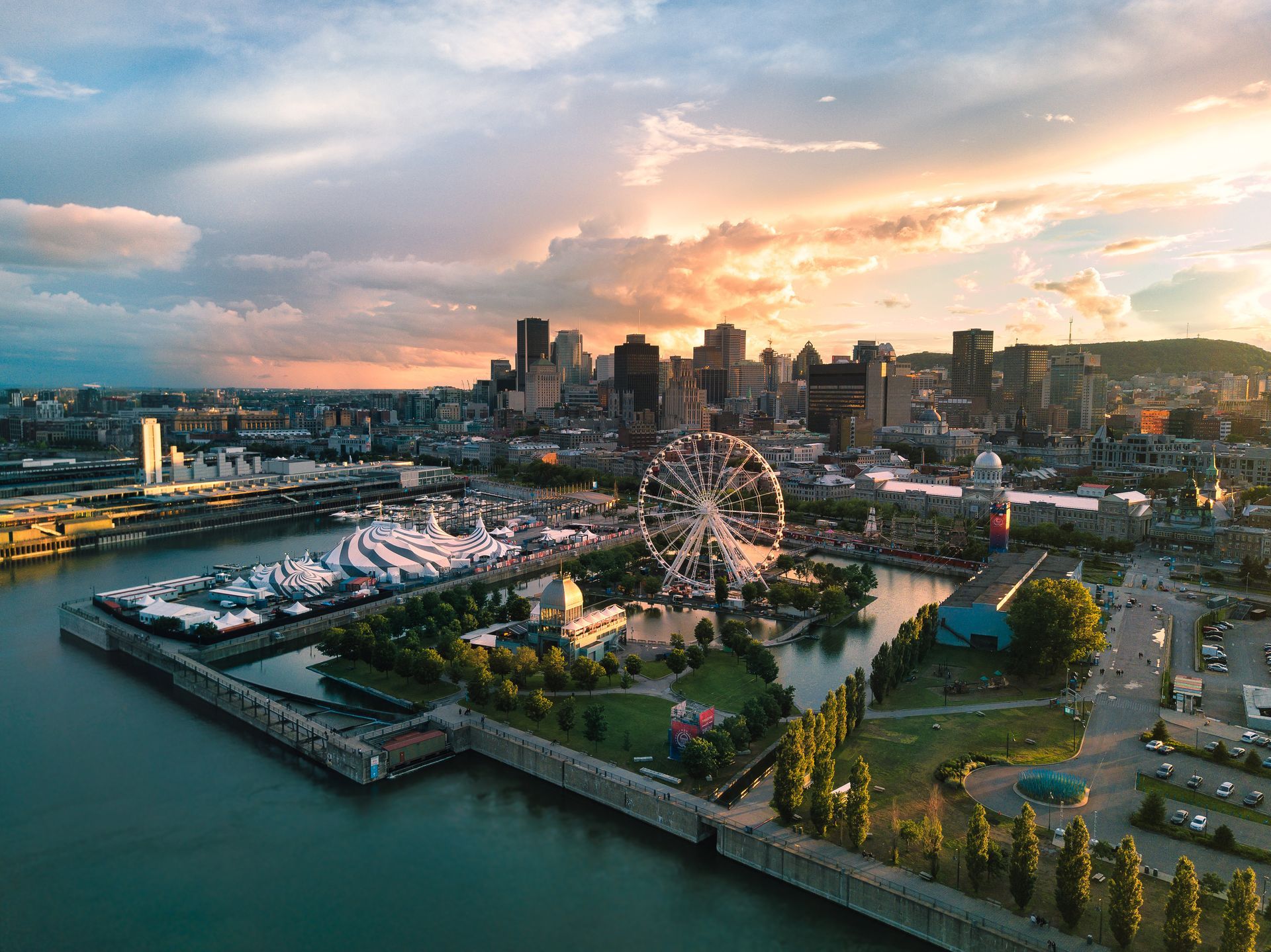 Luchtfoto van de skyline van Montréal aan het water bij zonsondergang, met een reuzenrad, jachthaven en park.