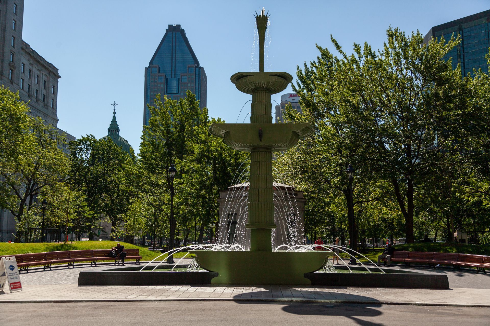 Stadspark in Montreal met een trapsgewijze fontein, bomen en hoge gebouwen onder een helderblauwe hemel.