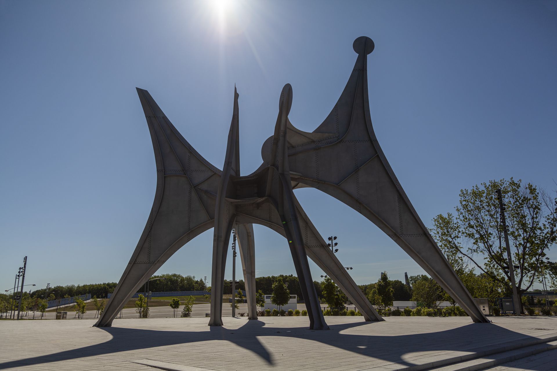 Grote, donkere, abstracte sculptuur in Montreal met gebogen steunpilaren op een zonnig buitenplein.