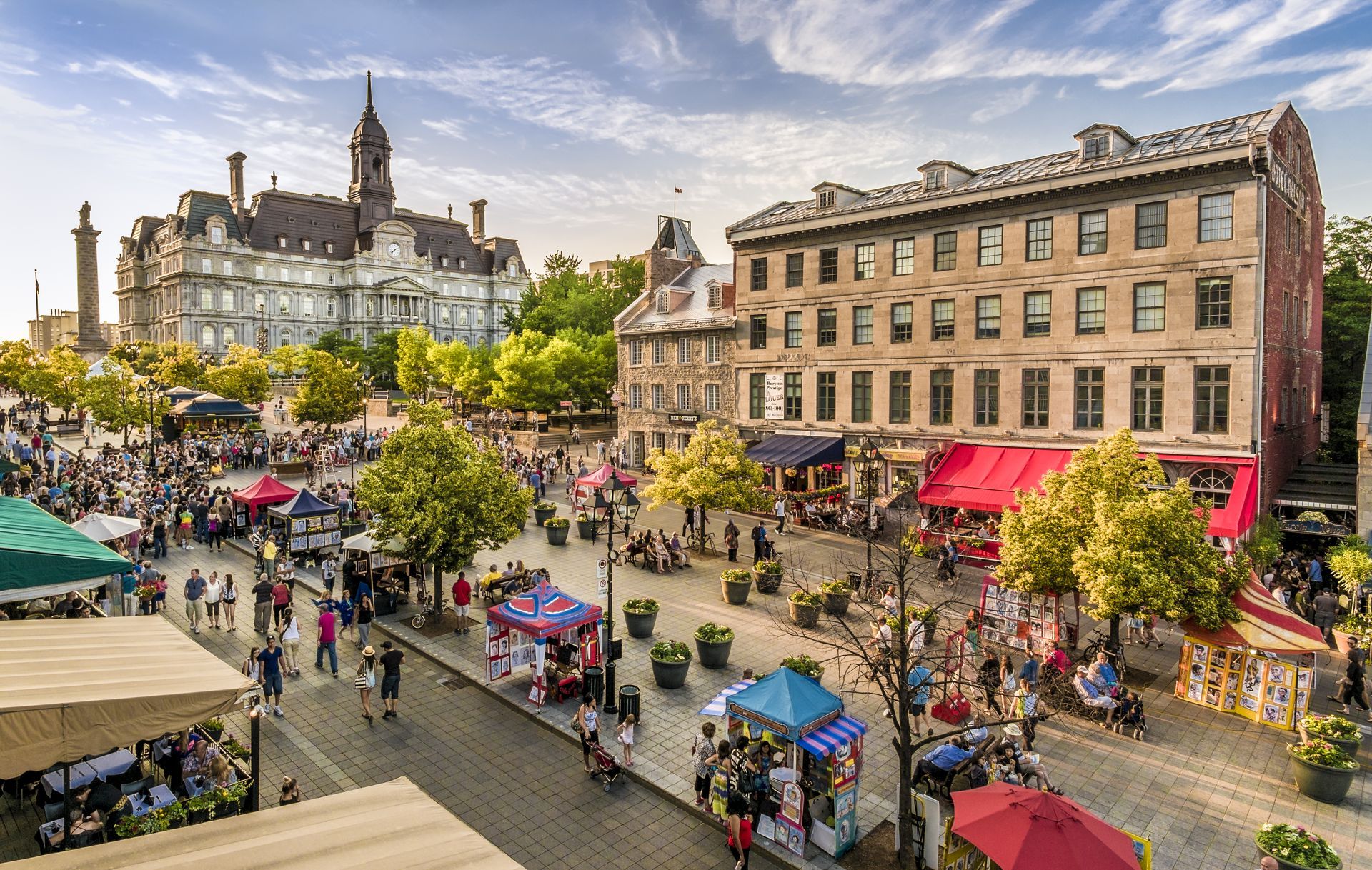 Een druk stadsplein in Montreal met marktkraampjes, bomen en historische gebouwen onder een bewolkte hemel.