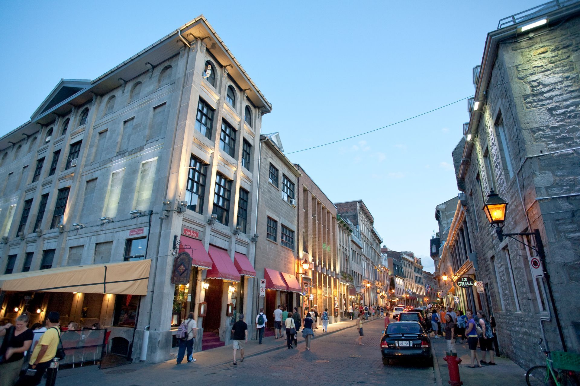 Een straat in Montreal met kinderkopjes, winkels en voetgangers in de schemering in een historische stadswijk.