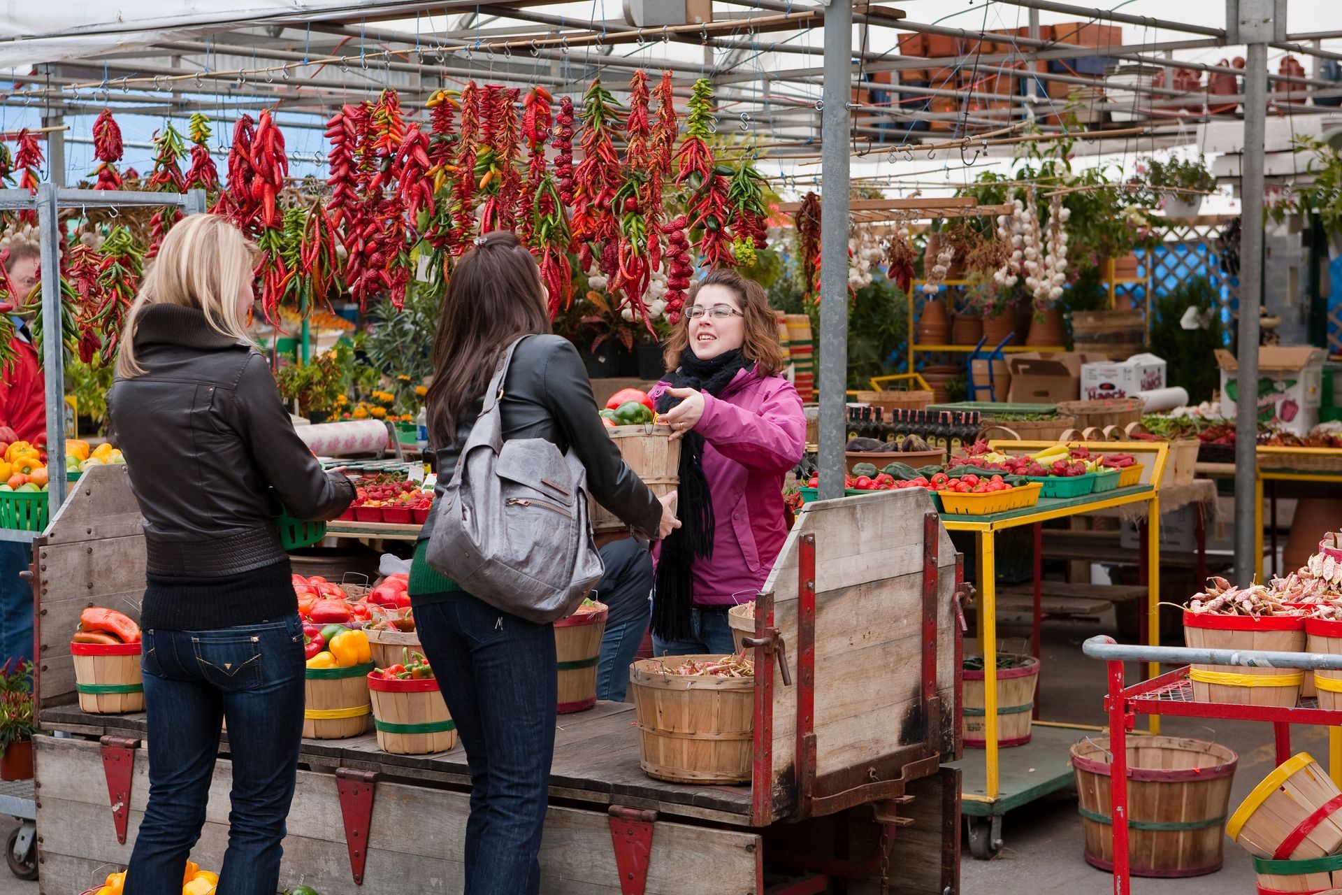 Mensen in Montreal bekijken een marktkraam met hangende rode paprika's en manden vol groenten en fruit.