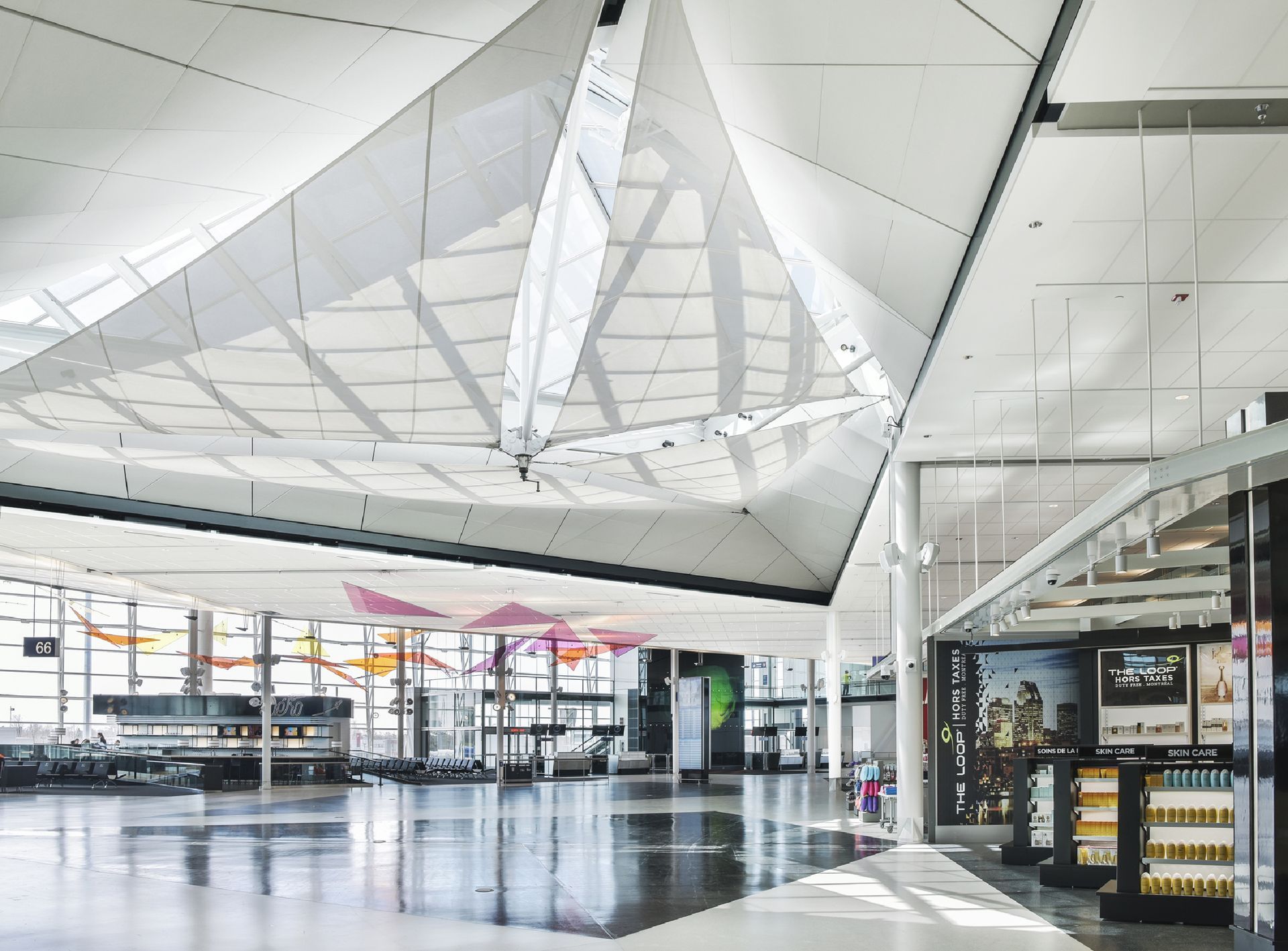 Modern interieur van een luchthaventerminal op Montréal International Airport met een hoog wit plafond, incheckbalies en gepolijste vloeren.