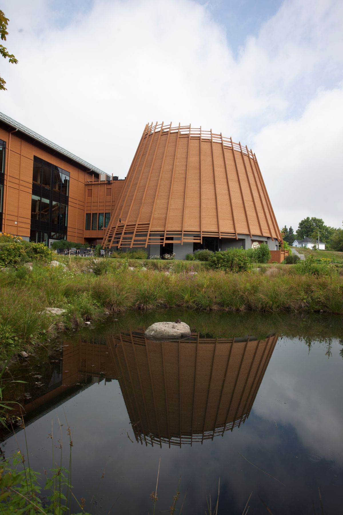 Modern houten gebouw van Musée Premières Nations in Canada met een kegelvormige gevel die weerspiegeld wordt in een vijver.