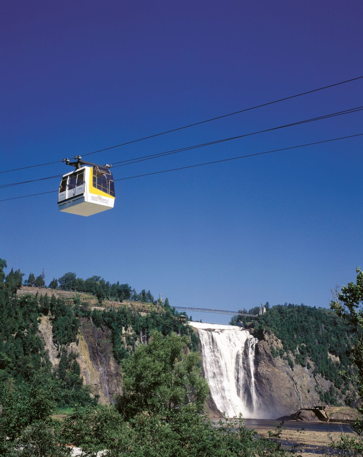 De kabelbaan over de waterval in Parc de la Chute-Montmorency in Canada en beboste kliffen onder een helderblauwe hemel.
