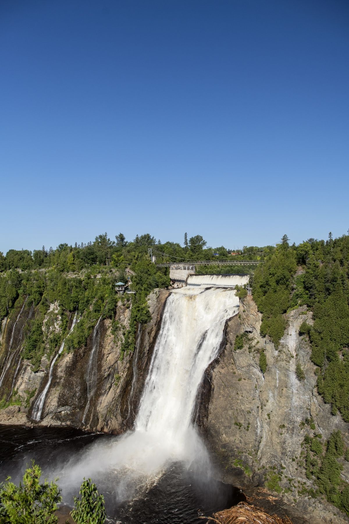 De waterval in Parc de la Chute-Montmorency in Canada die langs een rotsachtige klif naar beneden stort onder een helderblauwe hemel.