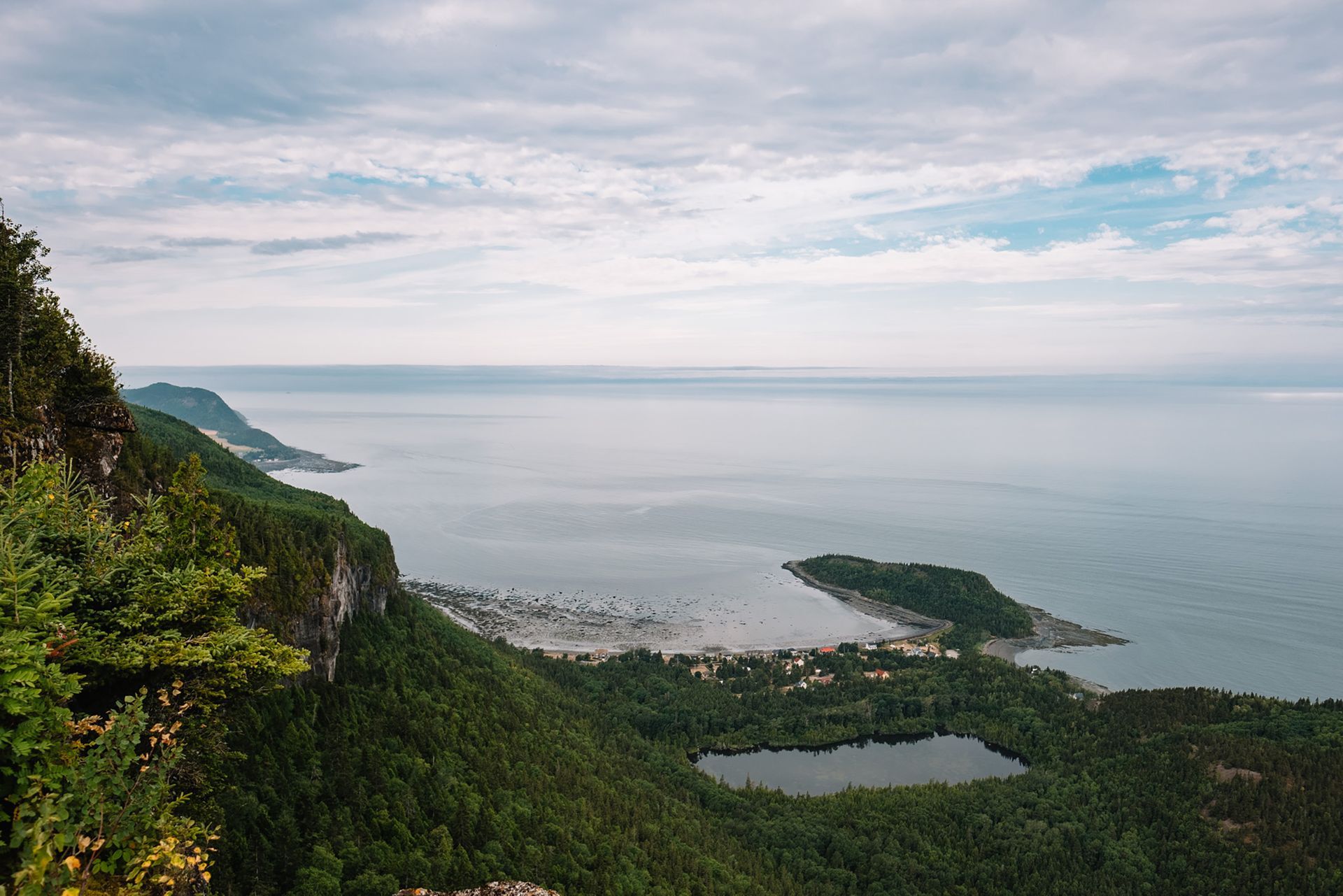 Weelderige groene kliffen van Parc national du Bic in Quebec, Canada, kijken uit over een kalme baai met een klein eiland en een bewolkte hemel.