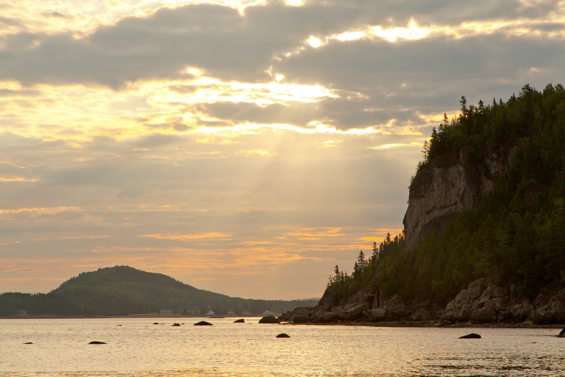 Gouden zonsondergang in Parc national du Bic in Quebec, Canada, boven een kalme zee met een rotsachtige klif en silhouetten van kleine eilandjes.