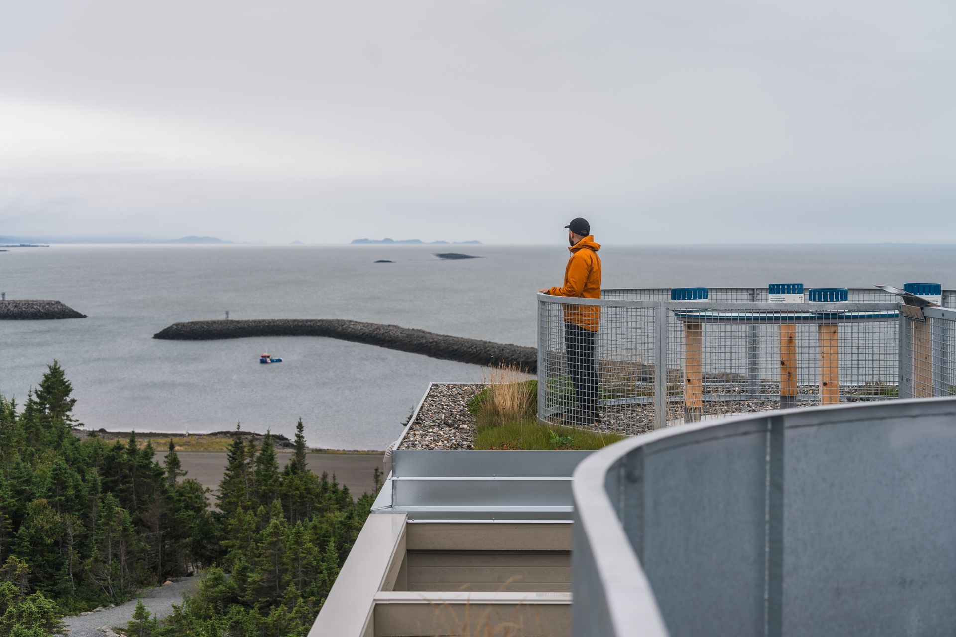 Persoon in oranje jas kijkt uit over de zee vanaf het uitkijkplatform van Putep ’t-awt Cacouna observation site in Quebec, Canada, aan de kust.