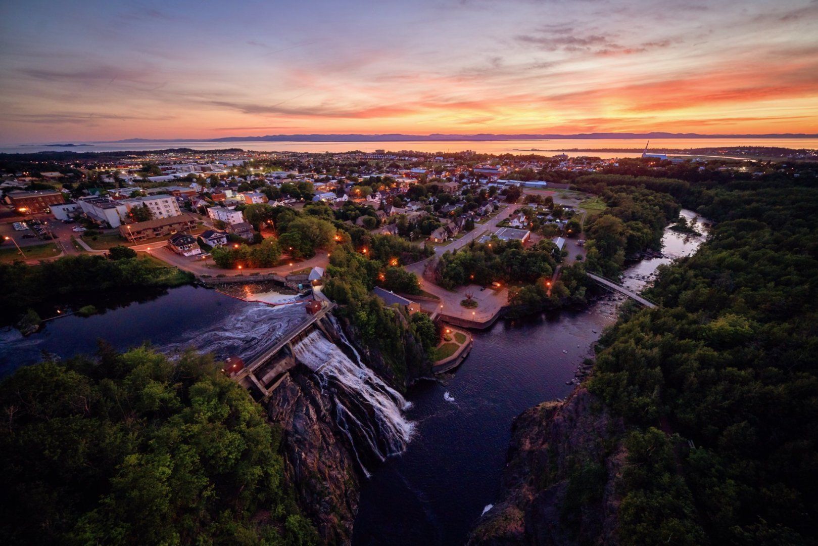 Luchtfoto van een zonsondergang met Parc du Chutes en Rivière-du-Loup in Quebec, Canada, tegen een roze-oranje hemel.