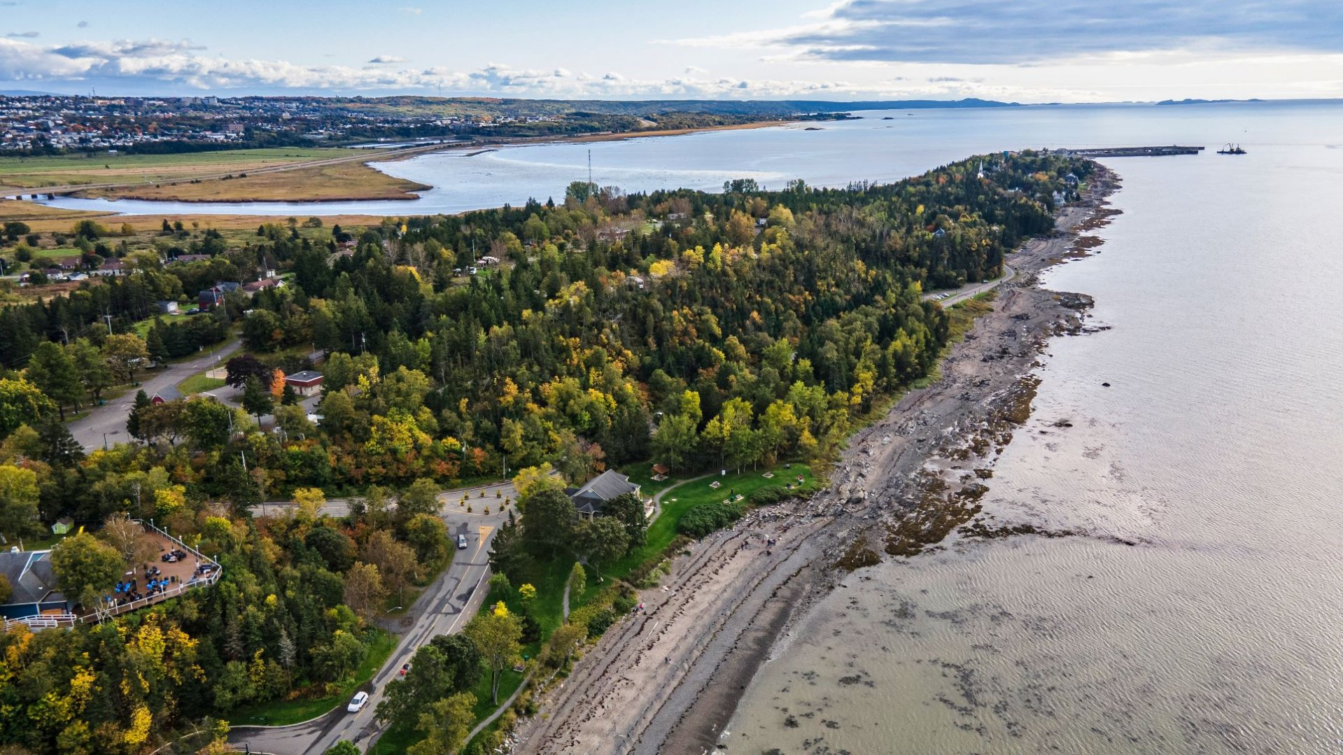Luchtfoto van een beboste oever langs een brede rivier met in de verte bergen en Riviere-du-Loup in Quebec, Canada, op de achtergrond.