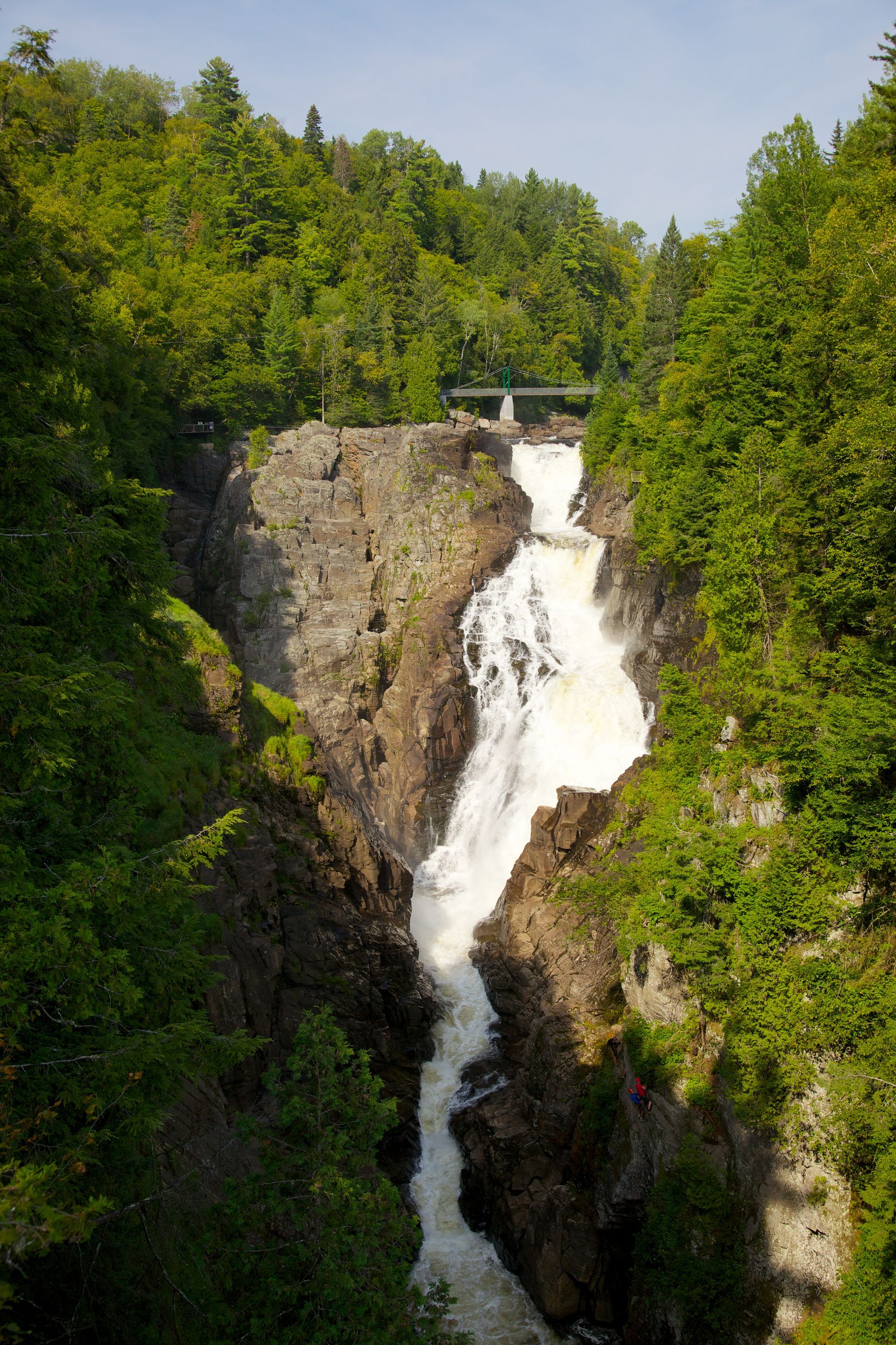 De hoge waterval van Canyon Sainte-Anne in Canada die door een rotsachtige kloof naar beneden stort, omgeven door weelderige groene bomen.