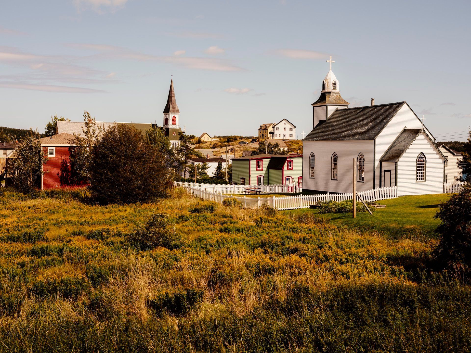 Witte kerk en dorpsgebouwen in Trinity, Newfoundland Canada, naast een moerassig veld onder een heldere hemel.