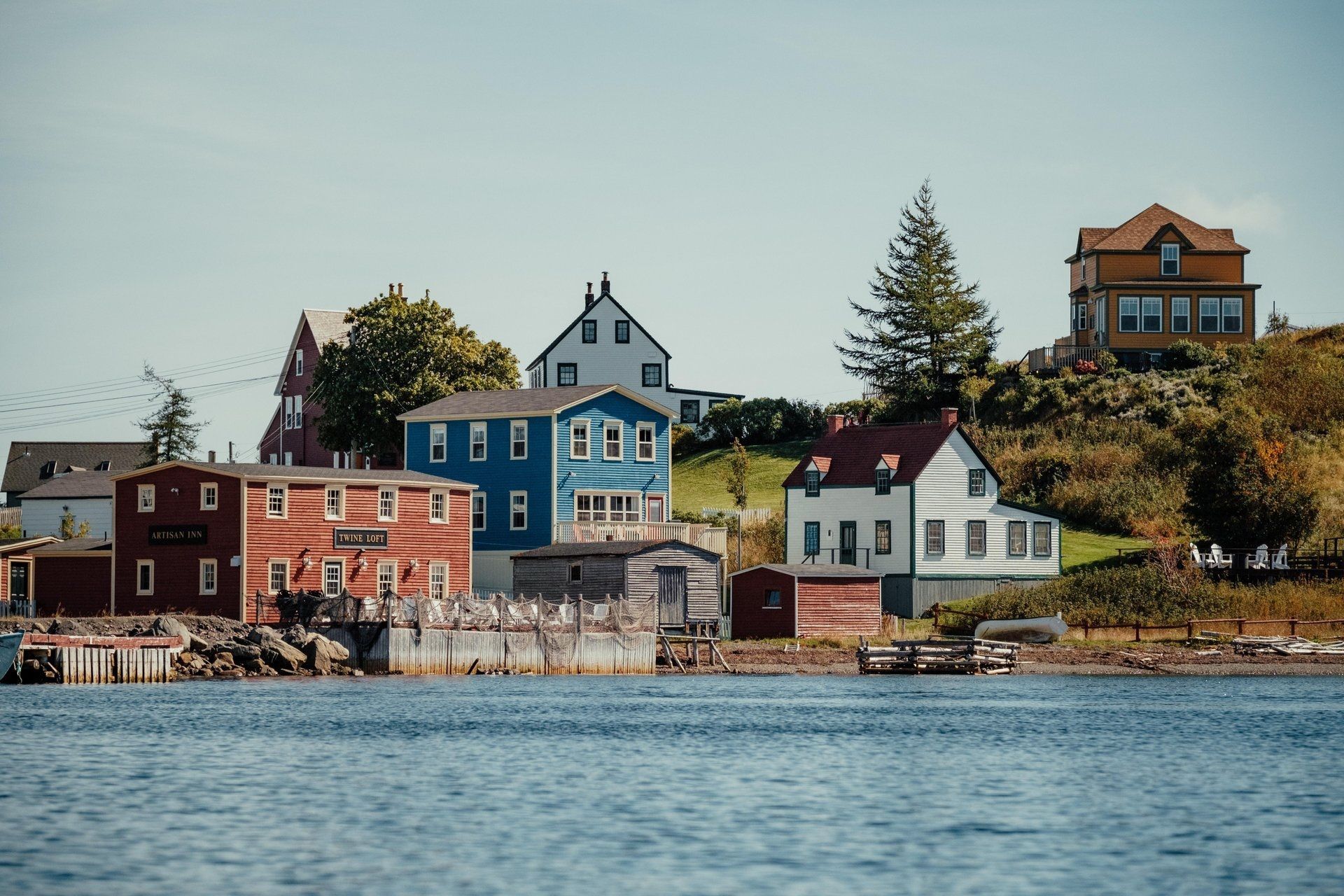 Kleurrijke huisjes in het kustdorpje Trinity, Newfoundland, langs een rotsachtige kustlijn met kalm water op de voorgrond.