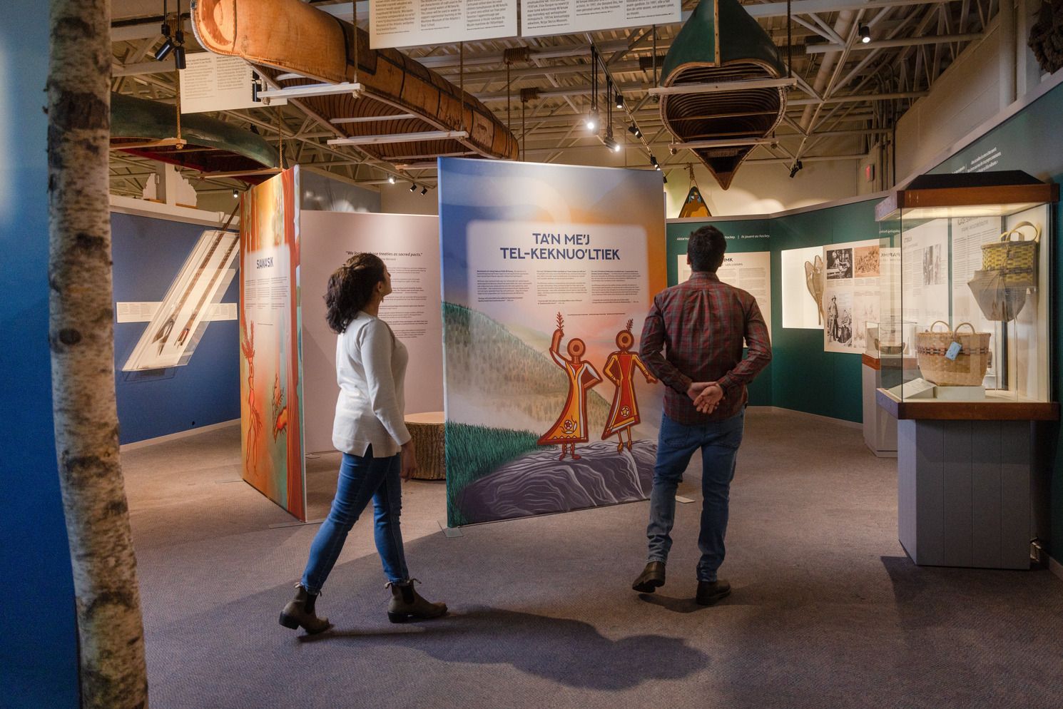 Twee mensen lopen door een museumtentoonstelling in het Maritime Museum of the Atlantic in Halifax met kleurrijke vitrines en artefacten.