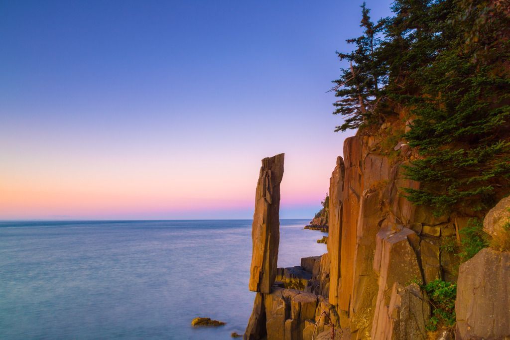 Balancing Rock op Nova Scotia bij zonsondergang met een kalme oceaan en een rozeblauwe lucht.