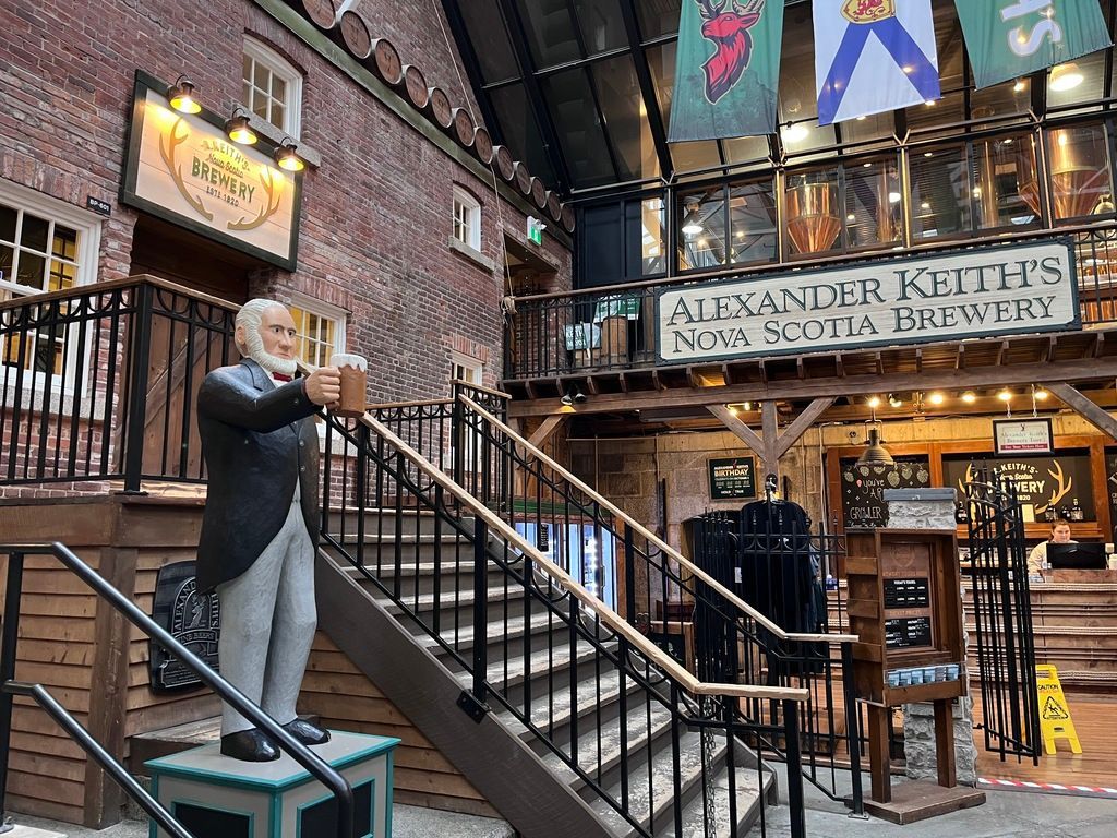 Een man in een zwarte jas speelt saxofoon op een trap in een bakstenen atrium, met hangende vlaggen en een uithangbord van een bar van een lokale bierbrouwerij in  Halifax op Nova Scotia, Canada.