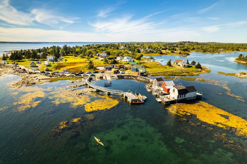 Luchtfoto van hutten en steigers van Blue Rocks op Nova Scotia  aan de oceaan op een klein eiland, omgeven door water en geel moerasgras.