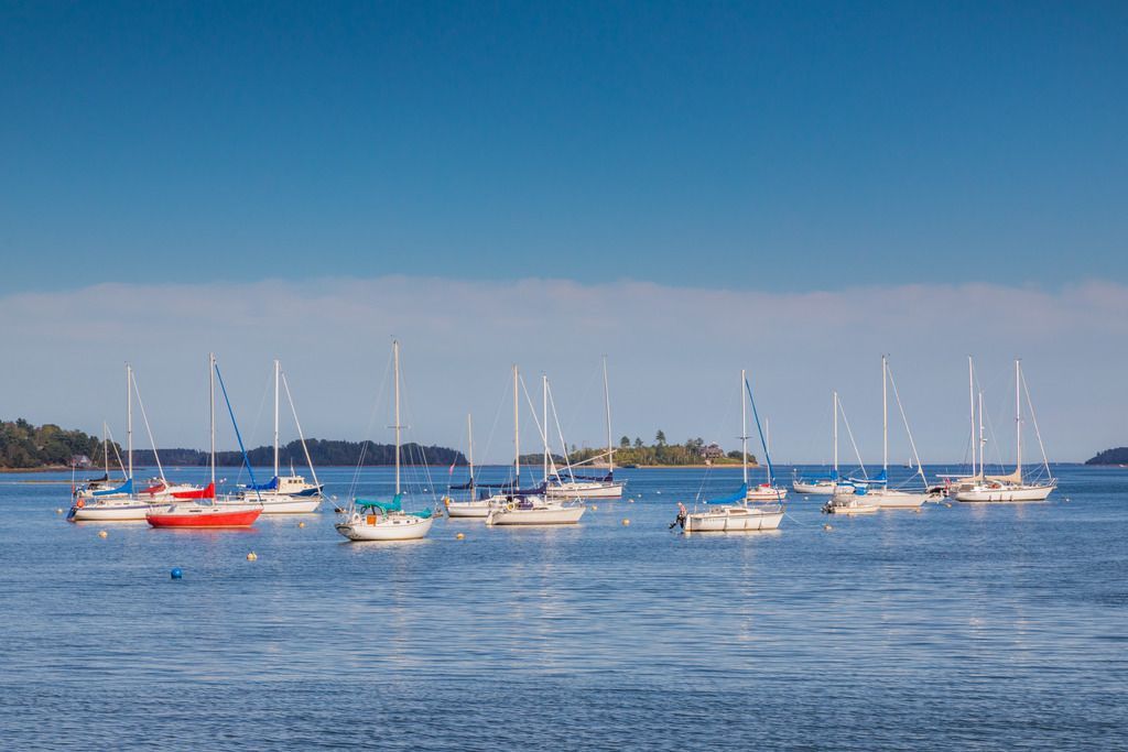 Zeilboten voor anker voor de kust van Mahone Bay op Nova Scotia op kalm, blauw water onder een heldere hemel.