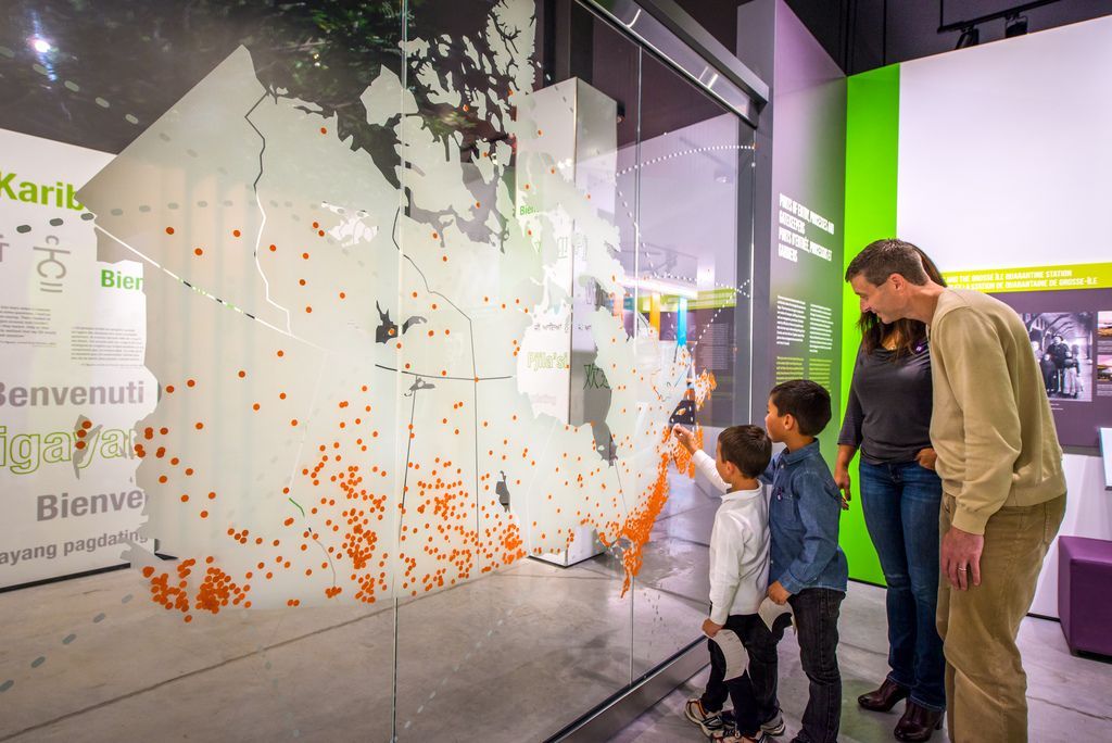 Mensen bekijken in het Canadian Museum of Immigration te Halifax op Nova Scotia, Canada, een grote interactieve tentoonstelling met abstracte witte en oranje afbeeldingen in een museumgalerie.