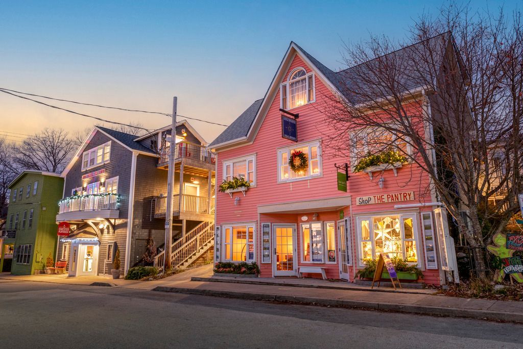 Kleurrijke winkelgevels en een roze huis in Chester op Nova Scotia dat bij schemering verlicht is in een rustige straat.