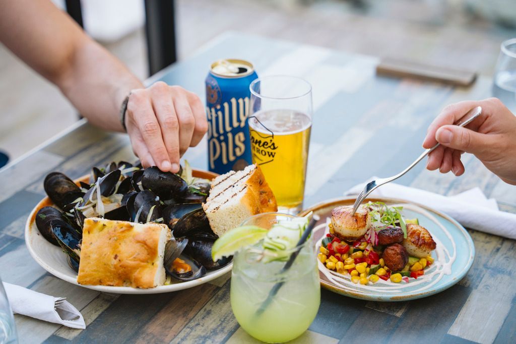 Handen reiken naar gedeelde schalen met mosselen, friet, salade en drankjes op een tafel buiten in Halifax op Nova Scotia, Canada.