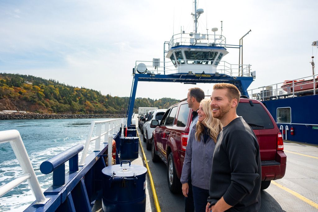 Passagiers staan ​​met auto's op het dek van de veerboot van Digby Neck naar Long Island, Nova Scotia, en kijken over het water richting de kust.
