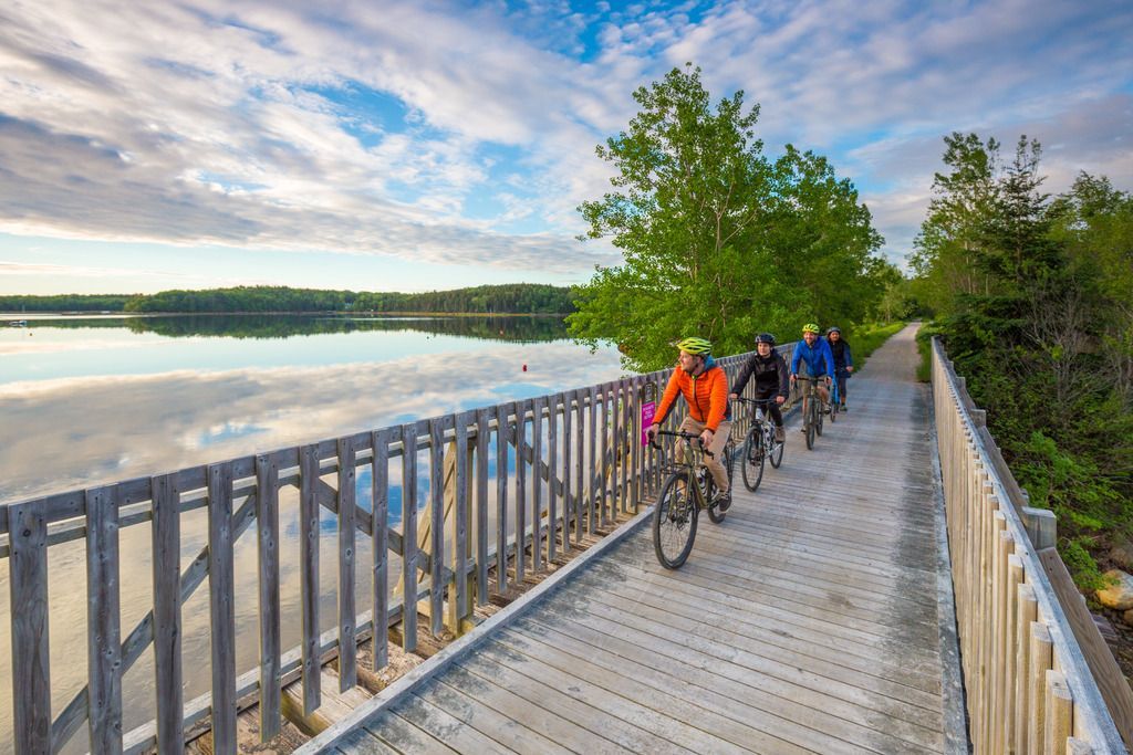 Fietsers rijden over een houten brug over een kalme oceaan onder een bewolkte hemel in de omgeving van Lunenburg, Nova Scotia.