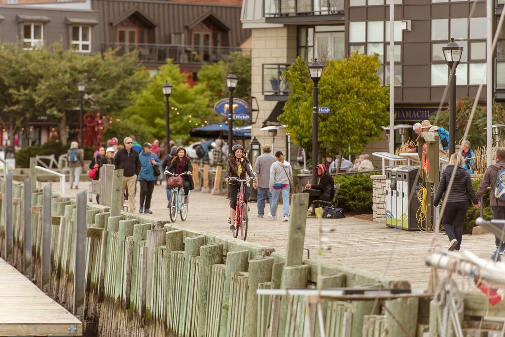 Een drukke wandelpromenade langs het water in Halifax op Nova Scotia, Canada, met mensen die onder een bewolkte hemel langs winkels en bloembakken slenteren.