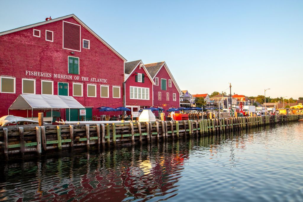 Rode gebouwen van Fisheries Museum of the Atlantic in Lunenburg, Nova Scotia, aan de waterkant langs een kade bij zonsondergang, met boten en weerspiegelingen op het kalme water.